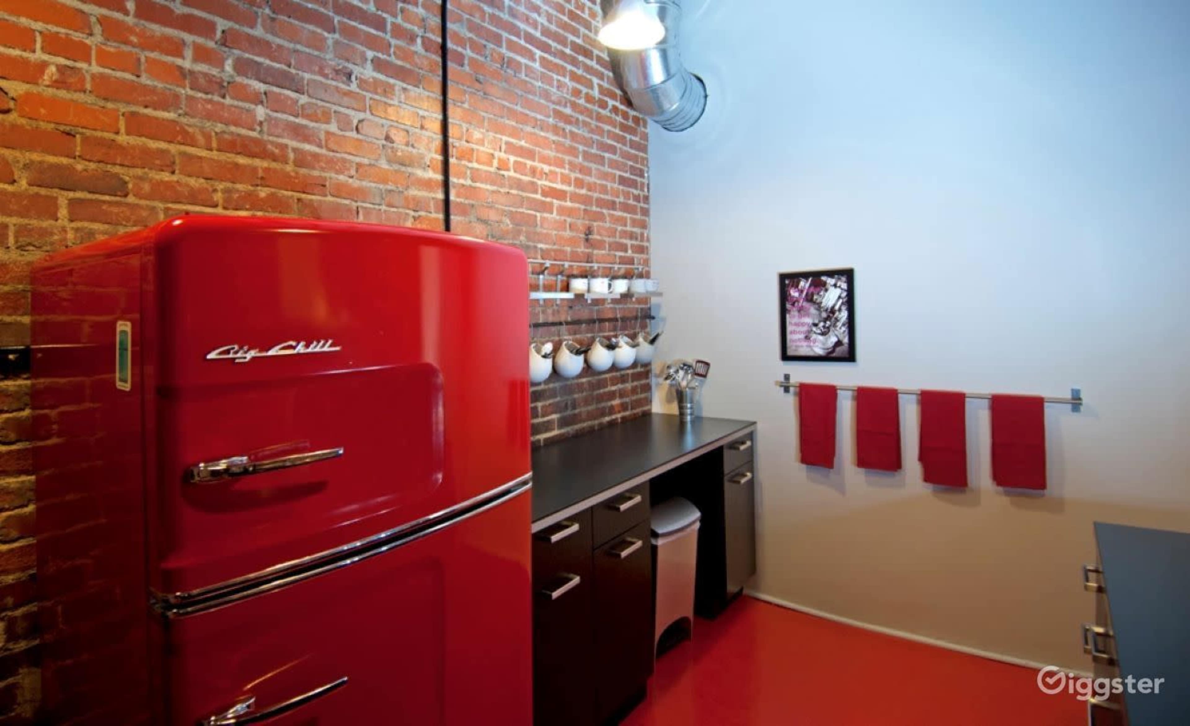 A red vintage refrigerator stands against a brick wall in a modern kitchen with gray countertops and red towels hanging on a rack.