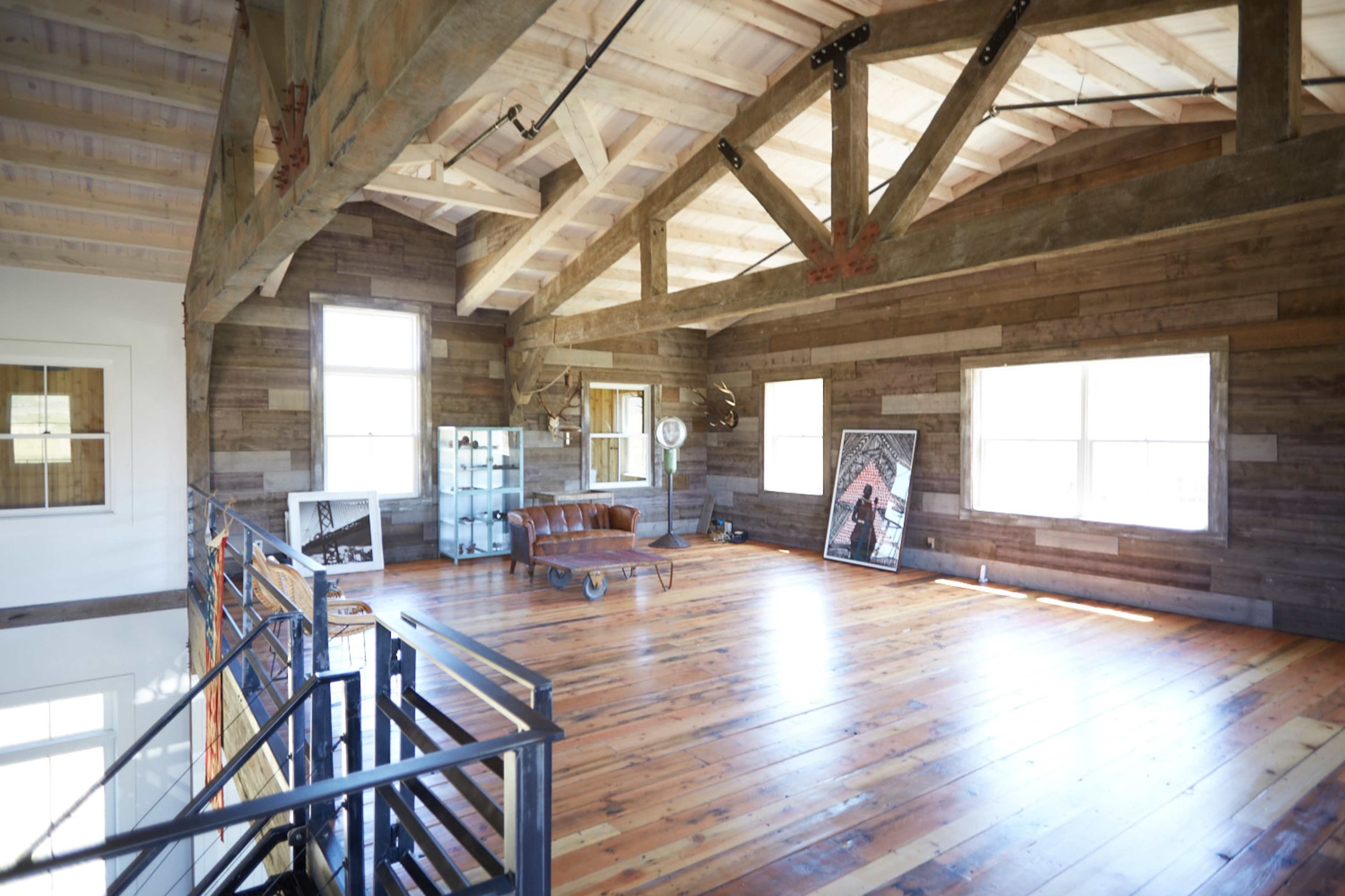 A spacious room with wooden walls, a high ceiling supported by beams, and a leather sofa placed near a large window.
