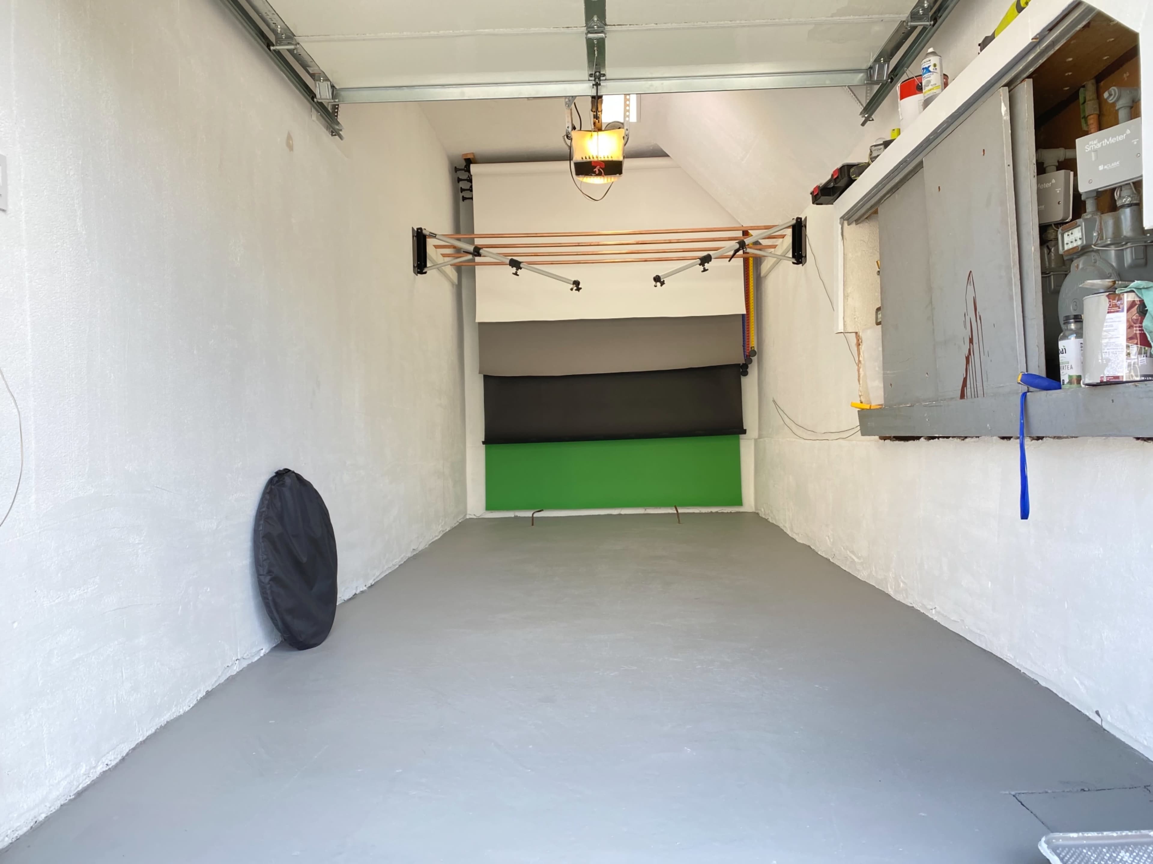 An empty garage with white walls, a gray floor, and a green backdrop at the far end.