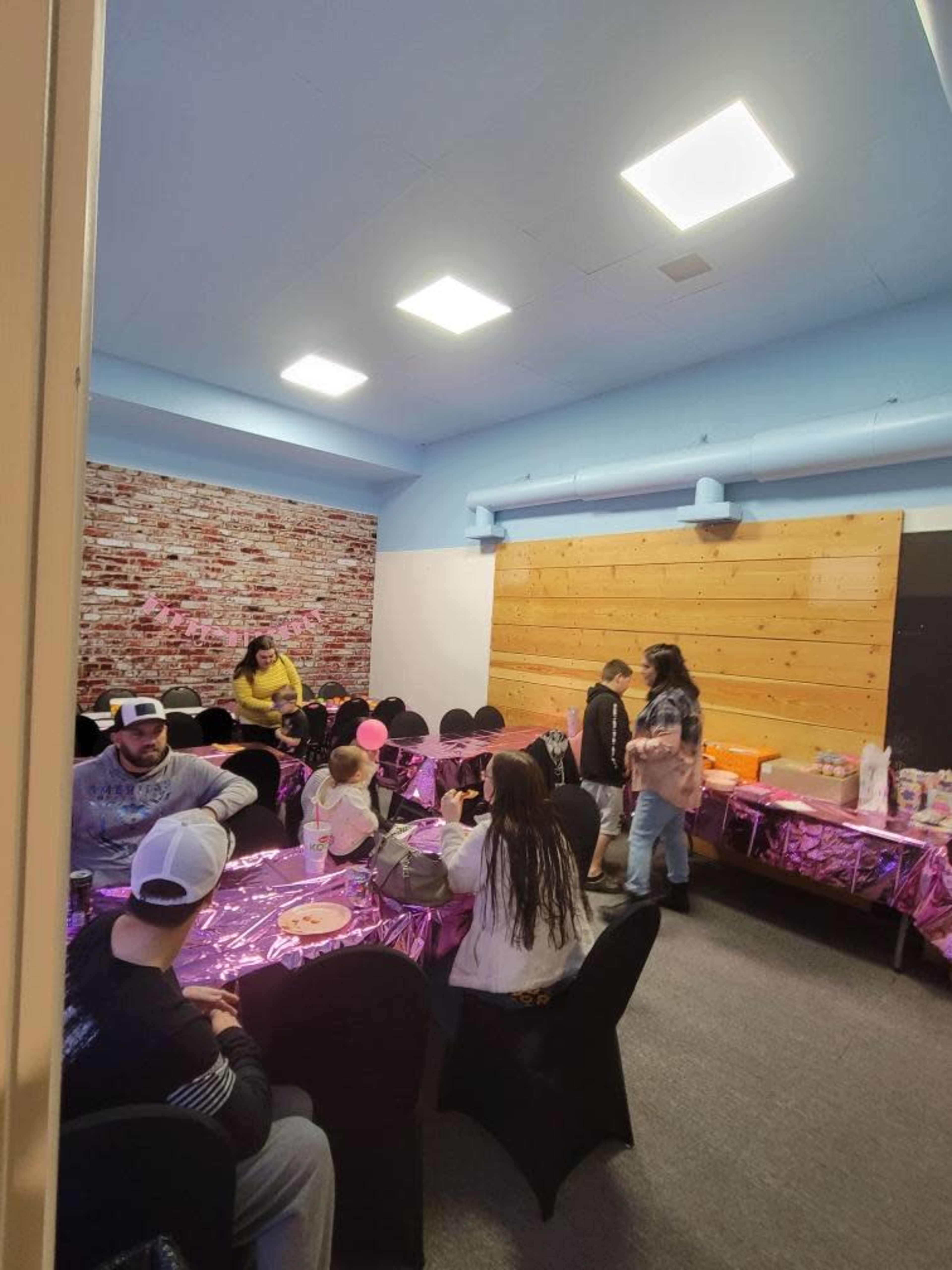 A decorated party room features tables covered in purple cloth with guests mingling and enjoying food.