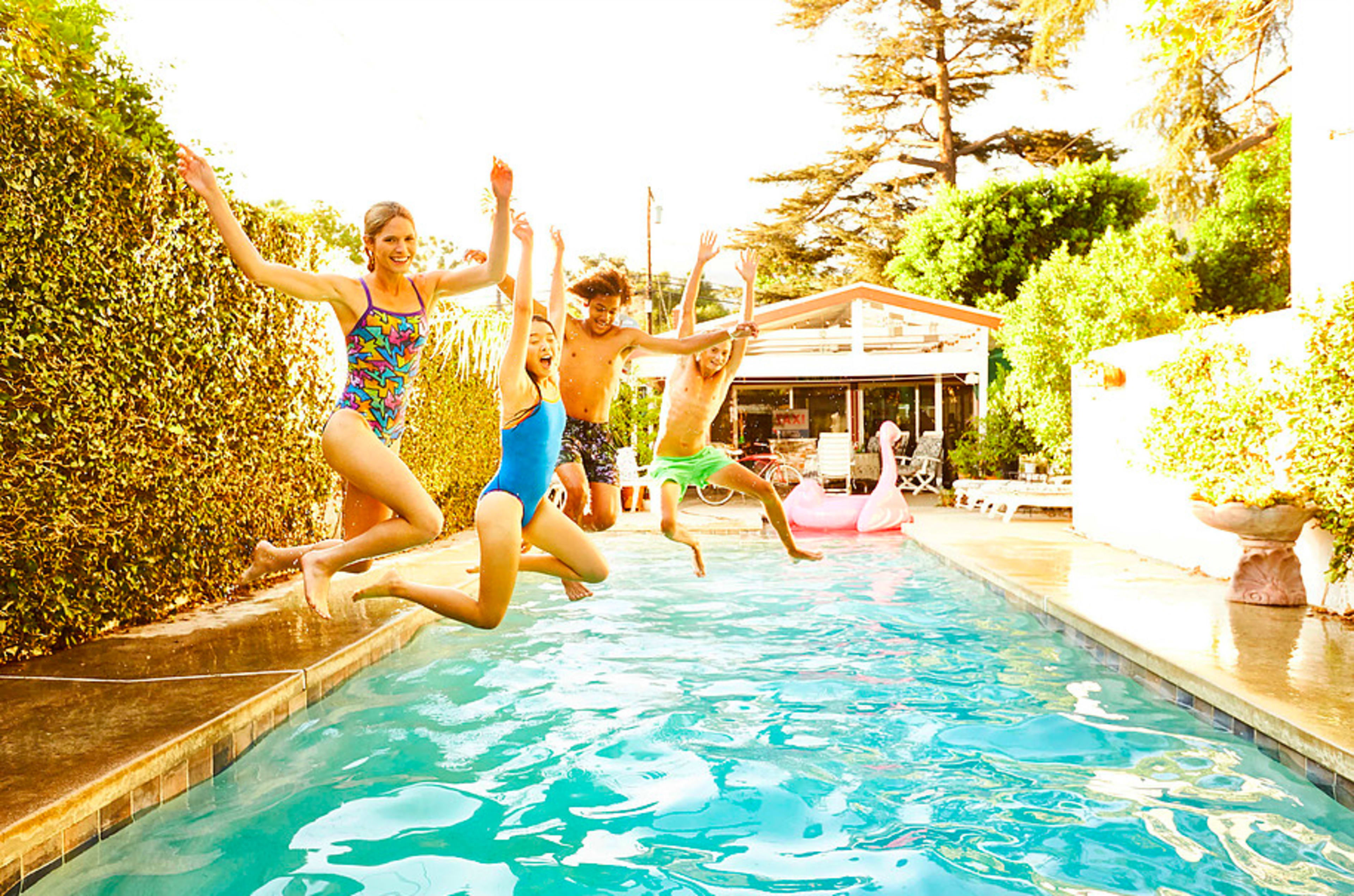 Four children jump into a swimming pool on a sunny day.