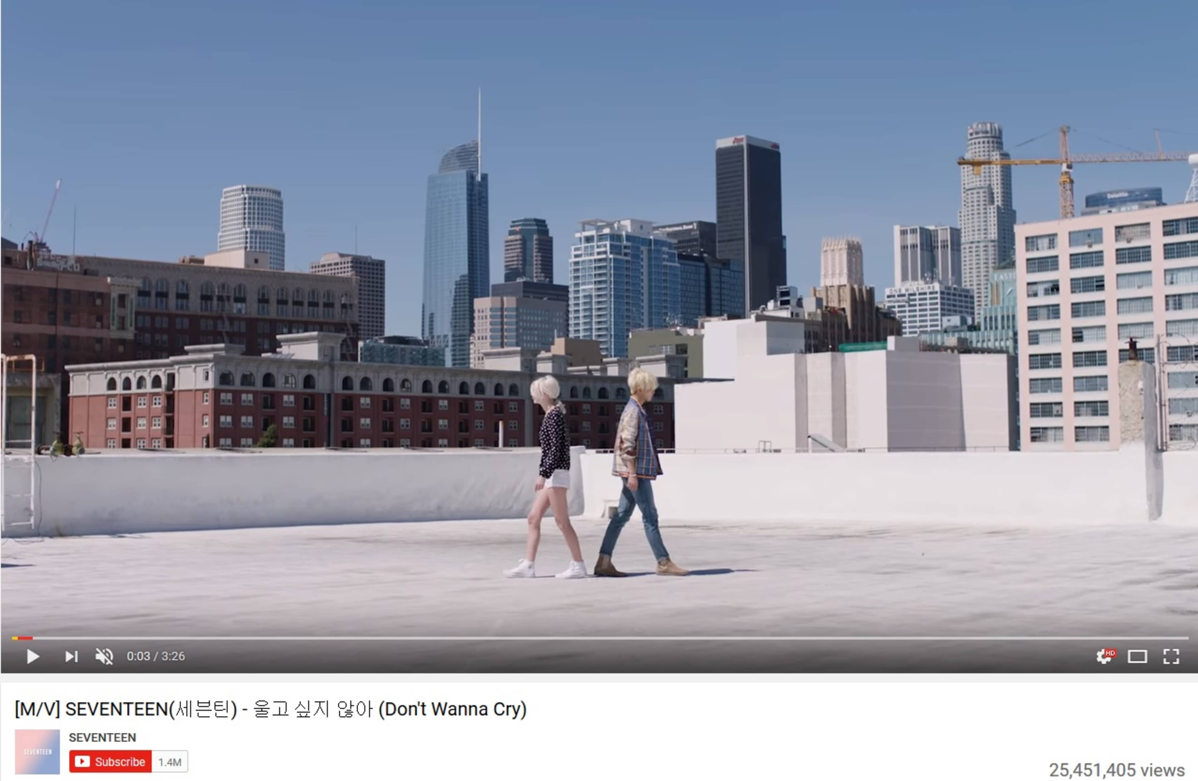 A boy and a girl walk side by side on a rooftop overlooking a city skyline with tall buildings.