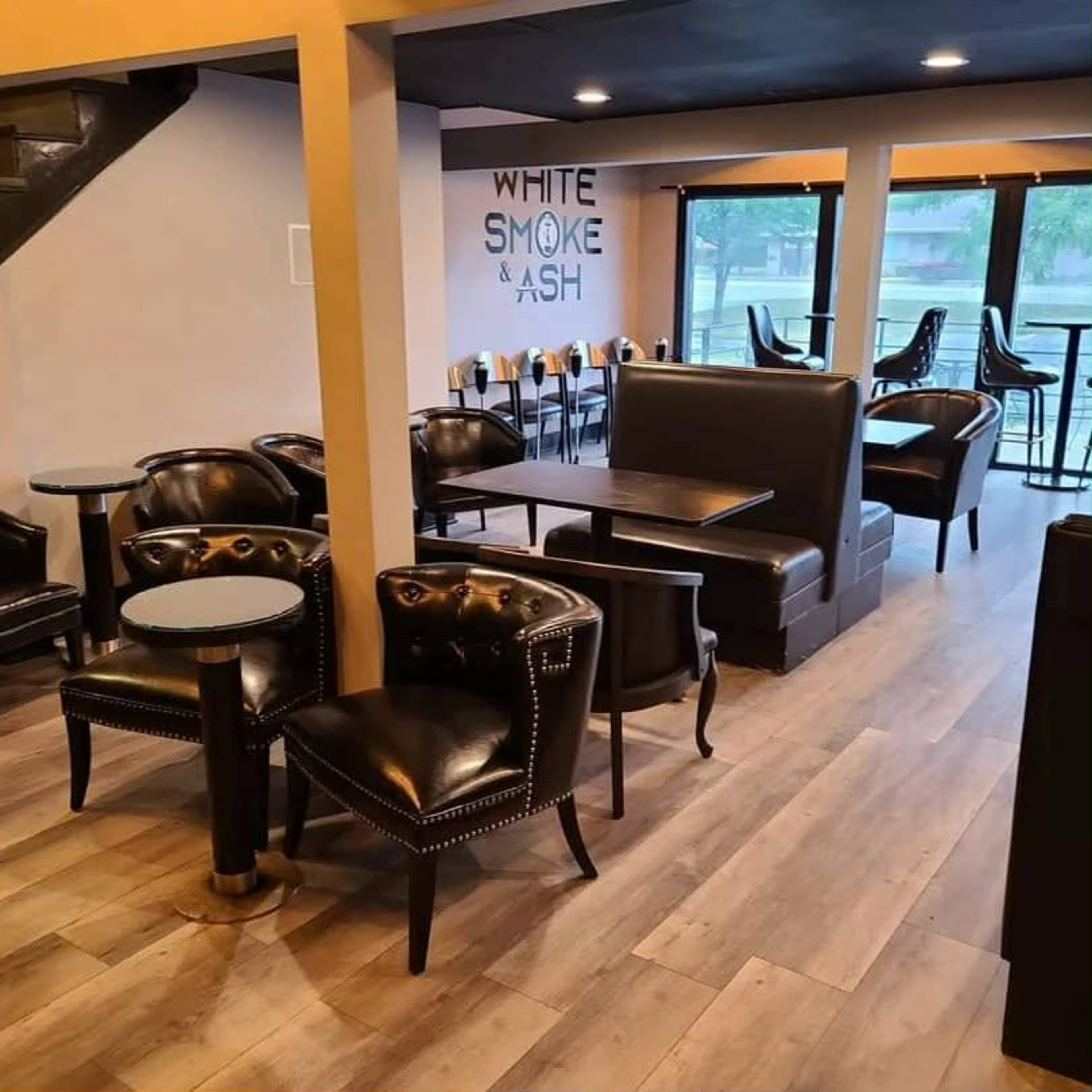 The image shows a modern café interior featuring black leather seating, wooden floors, and a wall with the text "WHITE SMOKE & ASH."