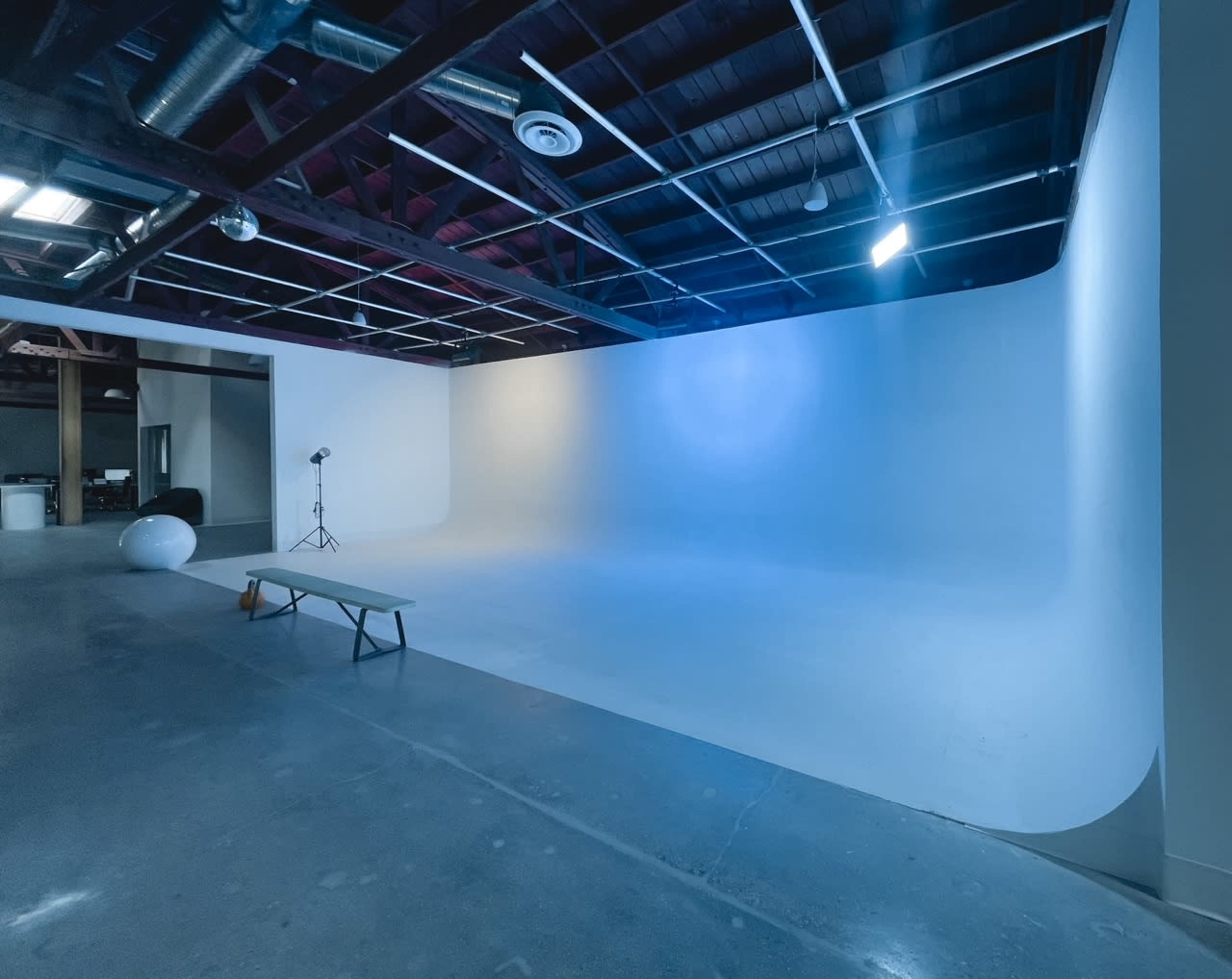 A spacious photography studio with a seamless white backdrop and minimal lighting equipment.