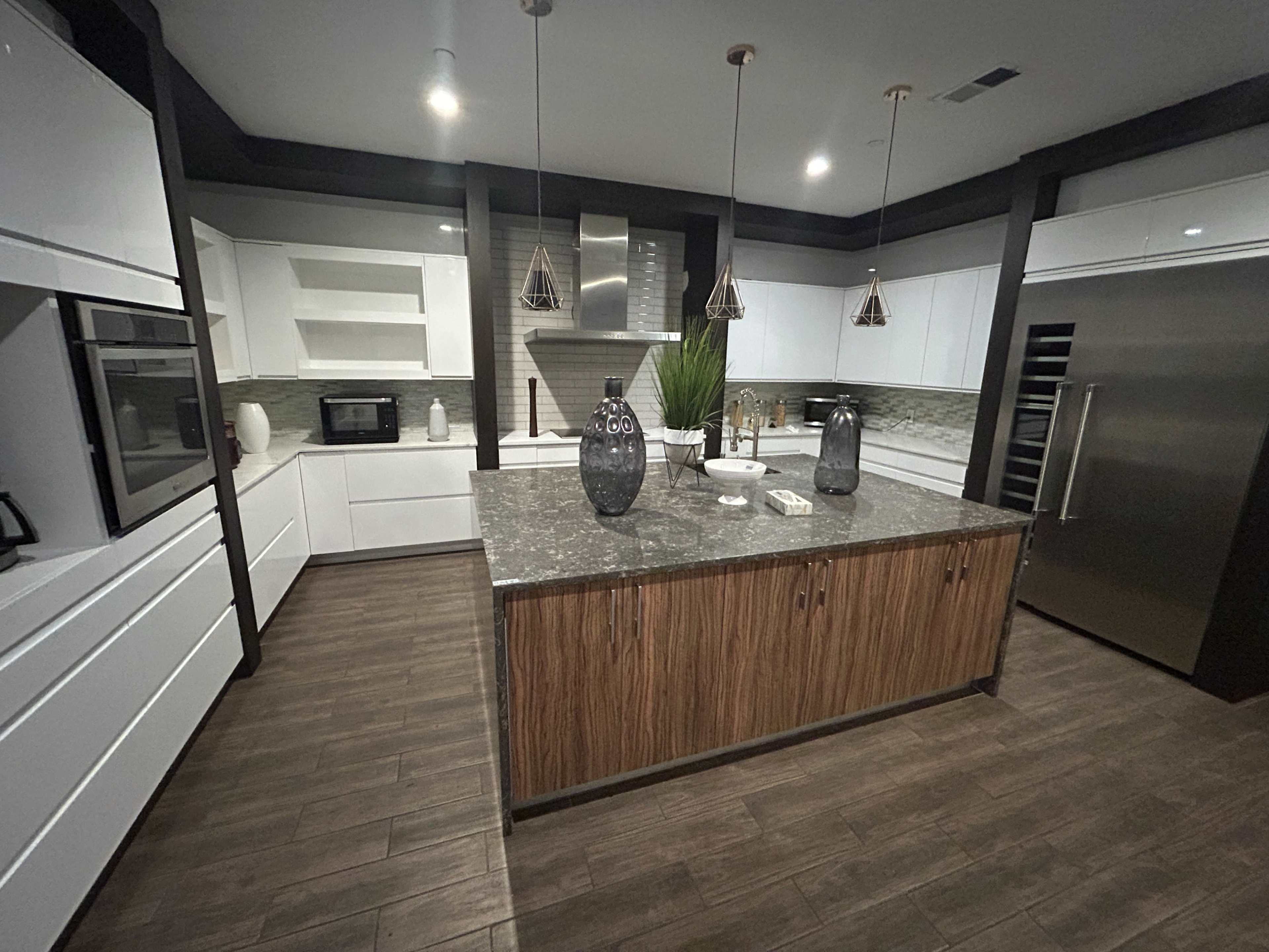 The image shows a modern kitchen featuring sleek white cabinetry, a central wooden island with a dark countertop, and pendant lighting above.