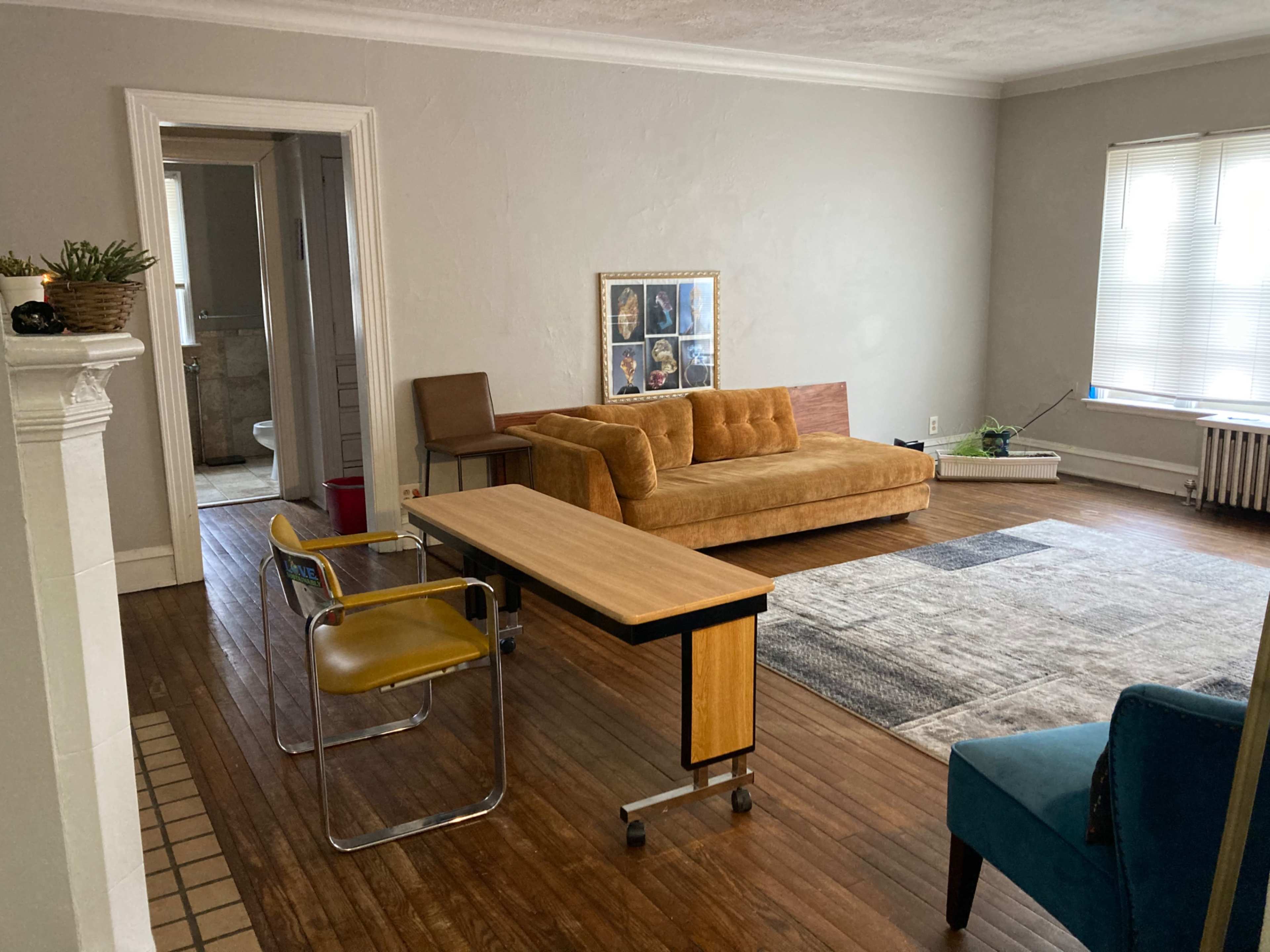 A living room with a brown couch, a small wooden table, and a chair, along with a blue armchair and wooden flooring.
