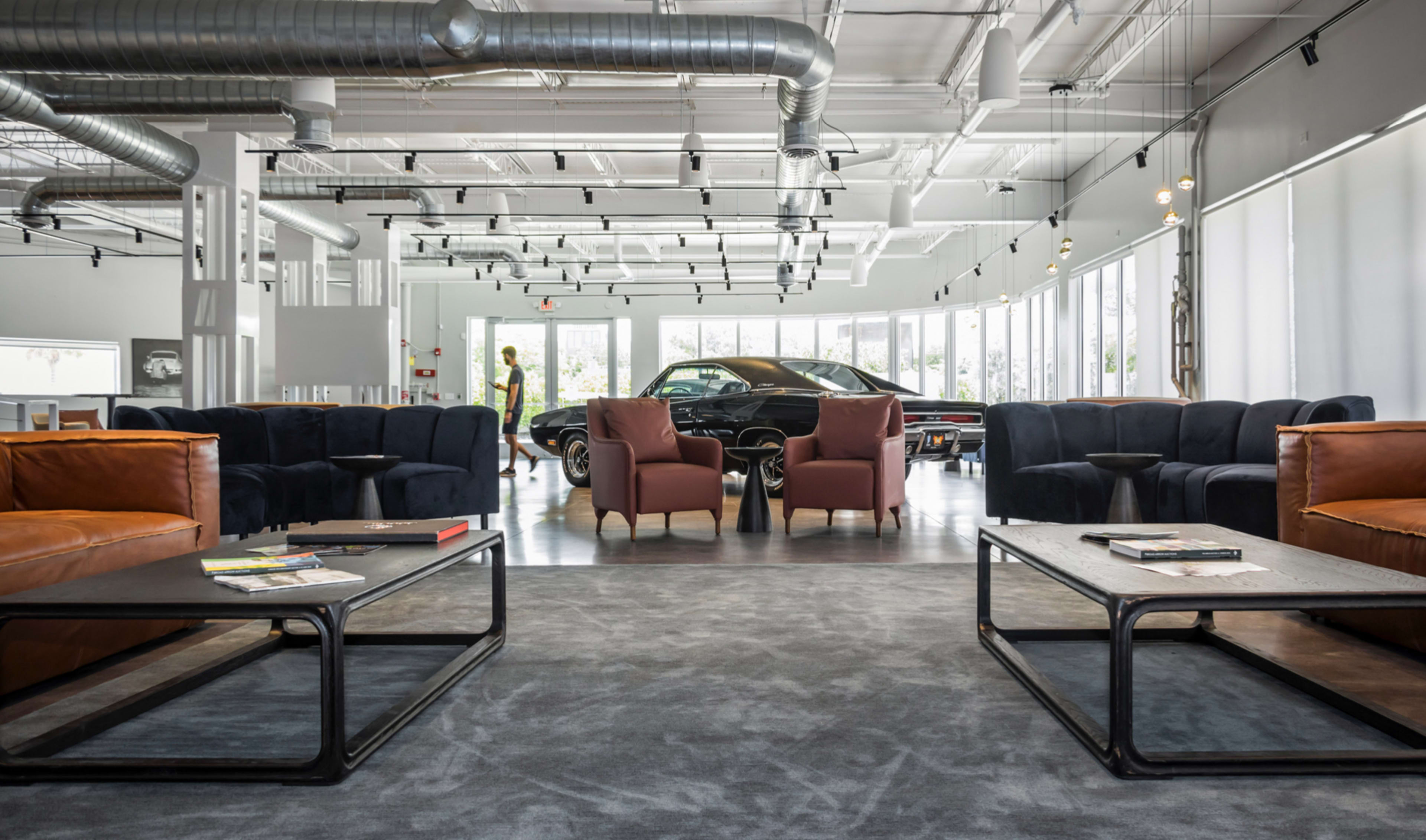 A modern, spacious lounge area with various seating arrangements and a classic car in the background.