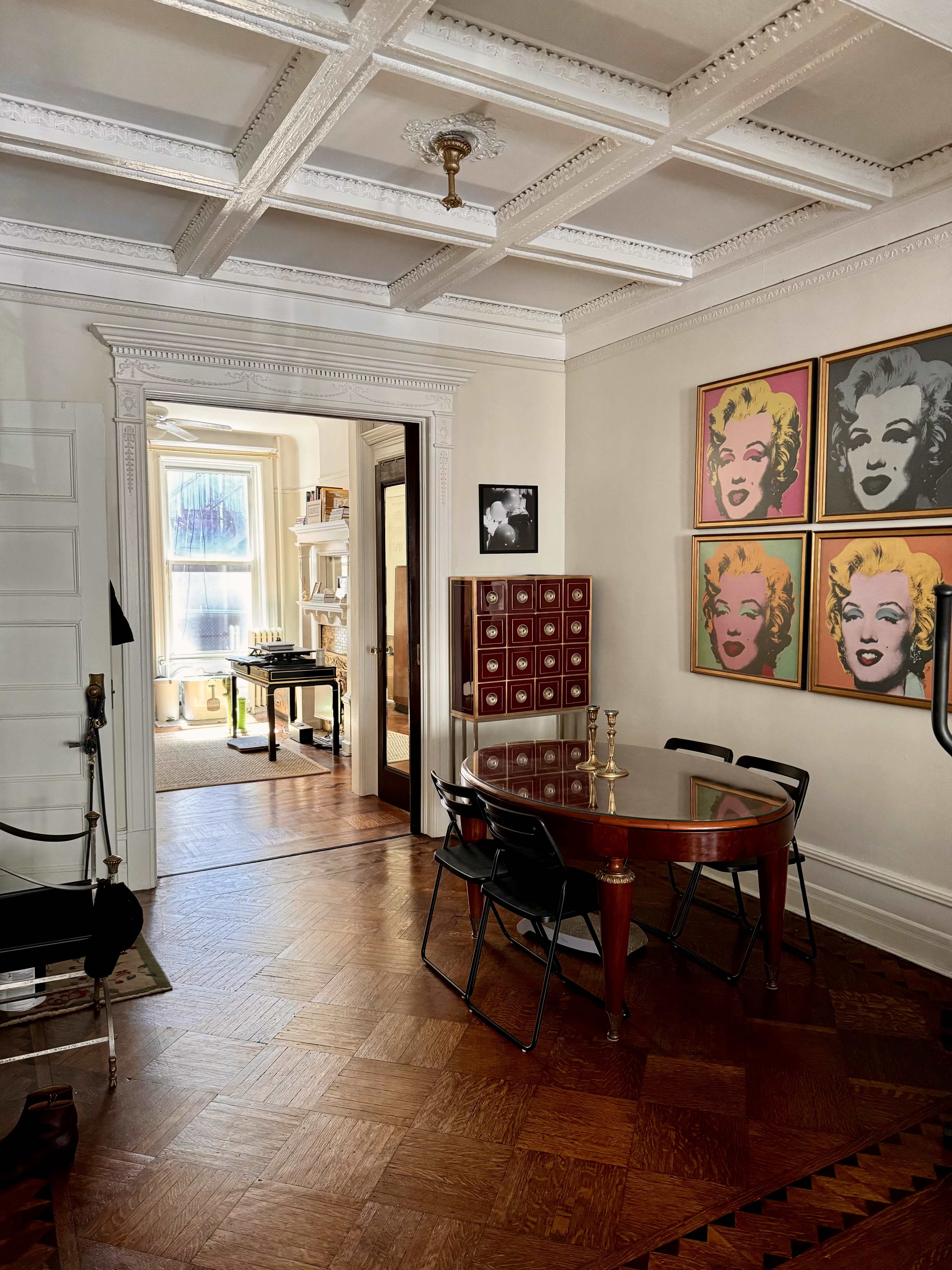 A well-lit room with a round dining table and chairs, a cabinet, and framed art featuring Marilyn Monroe on the walls.