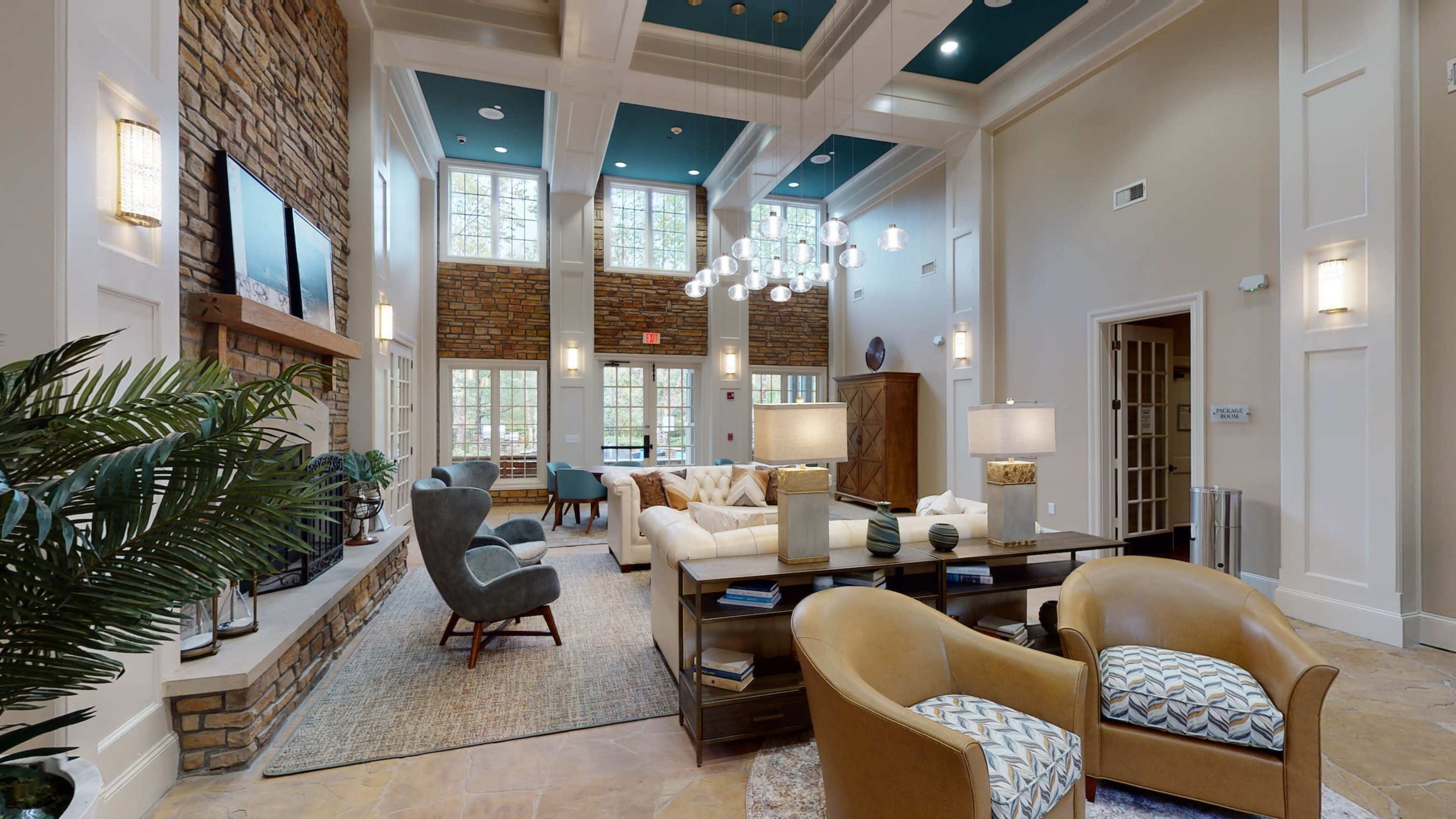 A spacious sitting area with a high ceiling, large windows, stone walls, and modern furniture arrangements.