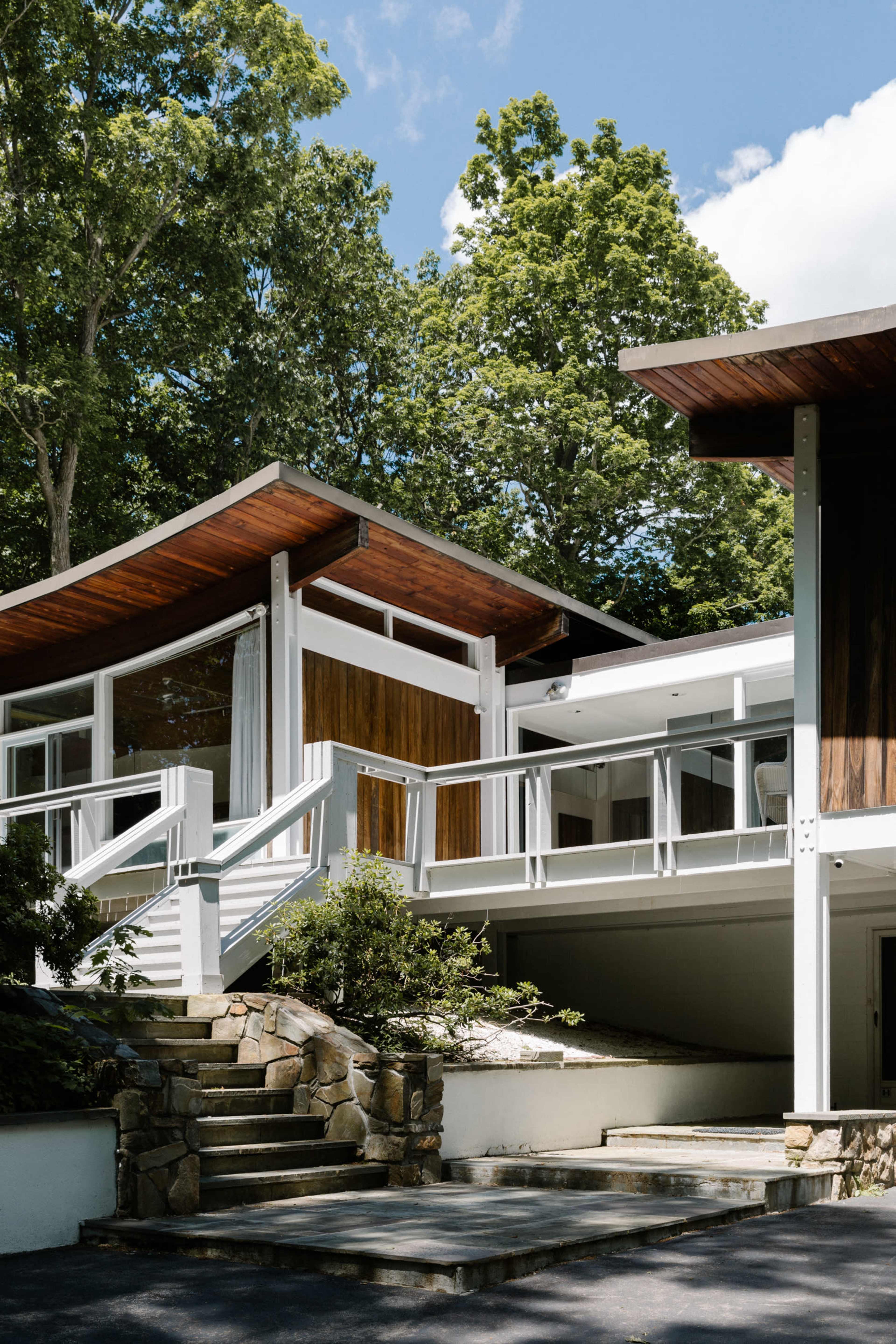 A modern house features a unique architectural design with curved roofs and large windows, surrounded by lush greenery.