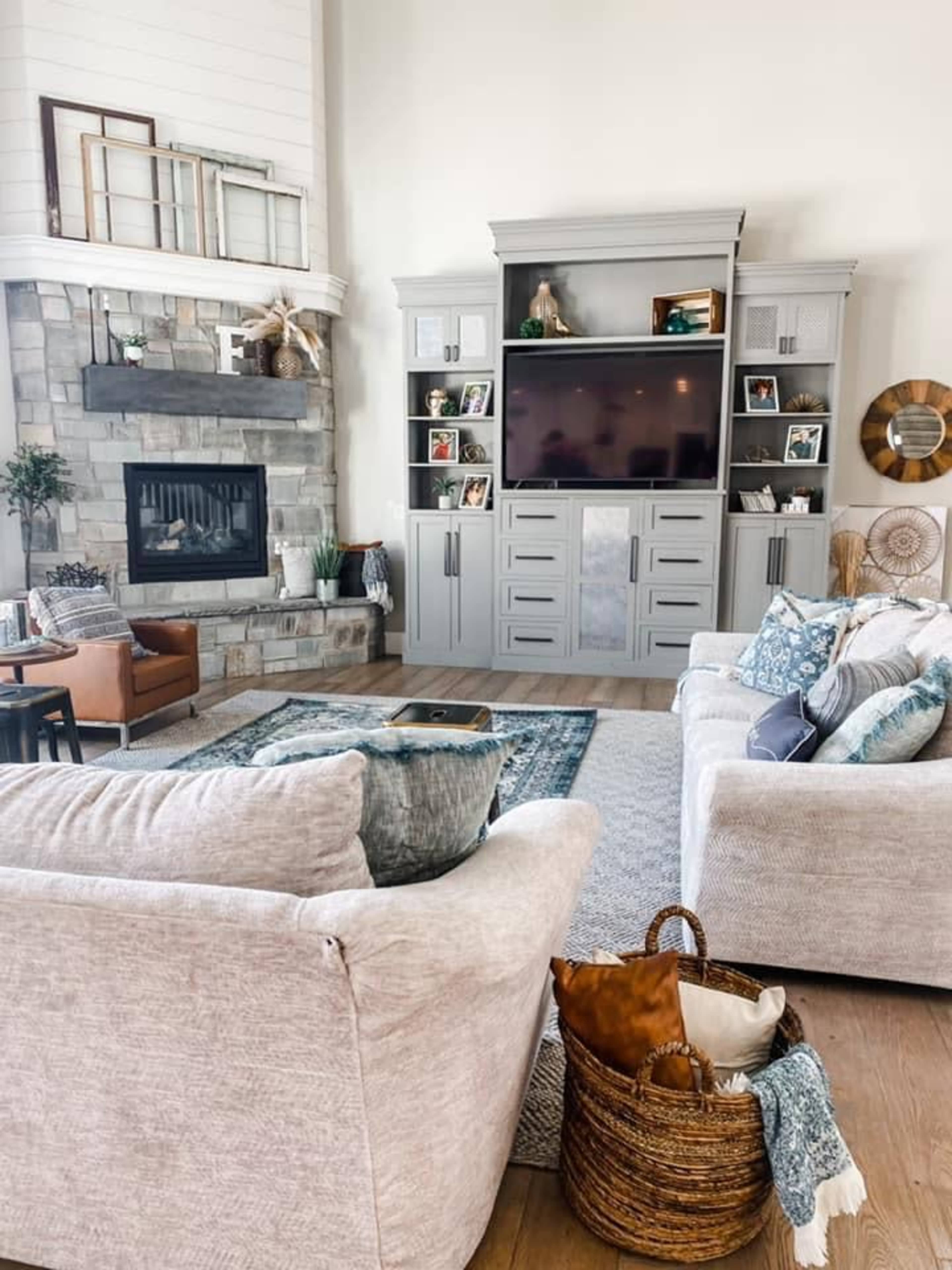 A cozy living room features two light-colored sofas, a wooden coffee table, and a stone fireplace with a television and shelves adorned with photos and decor.