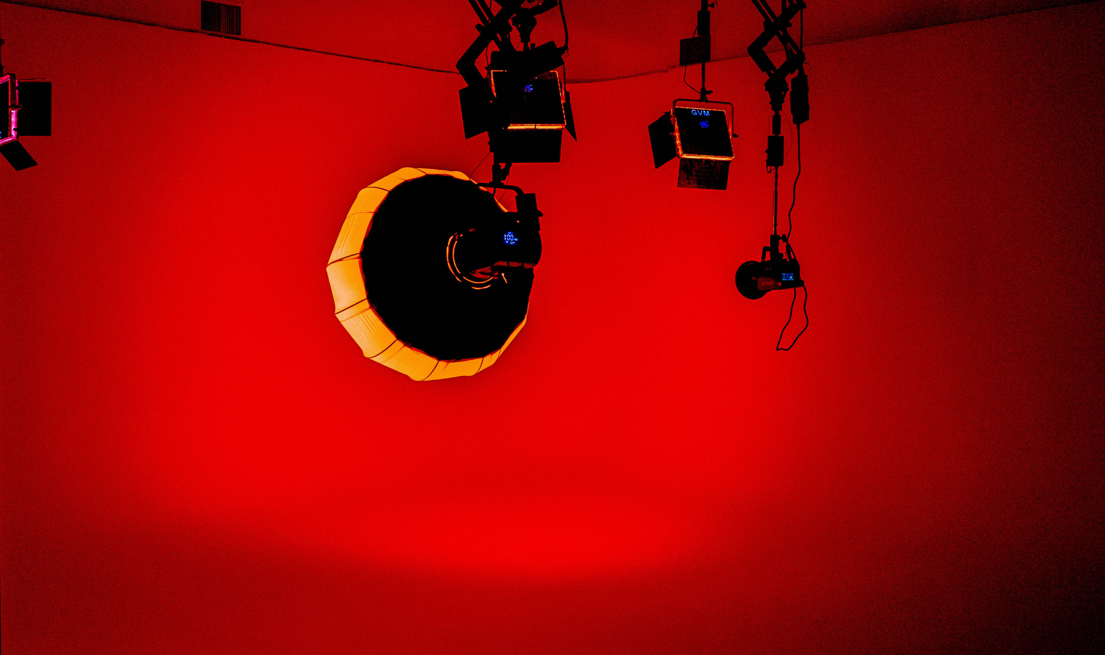 The image shows a red-lit studio scene featuring multiple overhead lighting fixtures directed towards a central light source with a circular design.