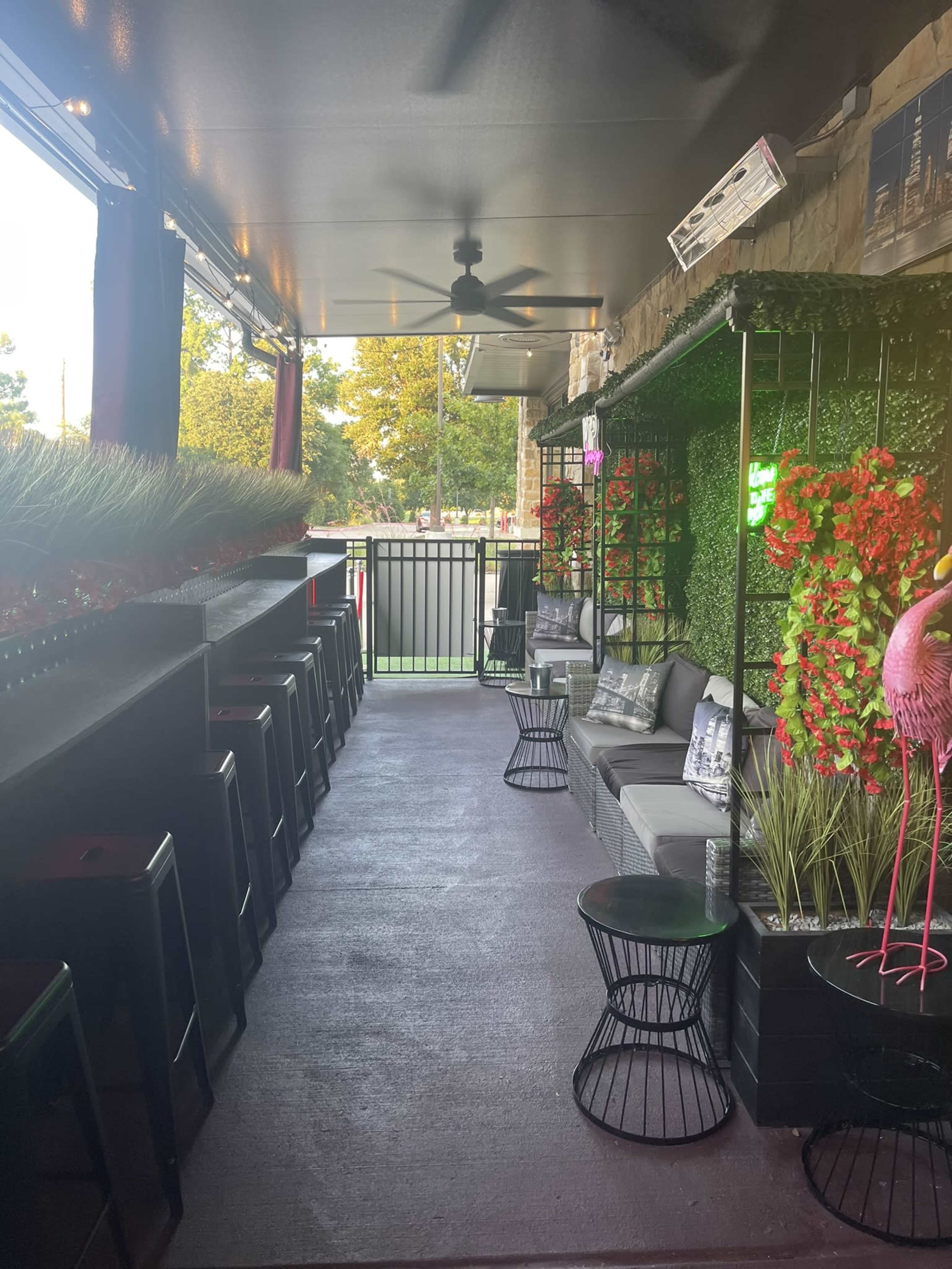 A restaurant patio area with dark seating, greenery, and decorative flowers along the walls.