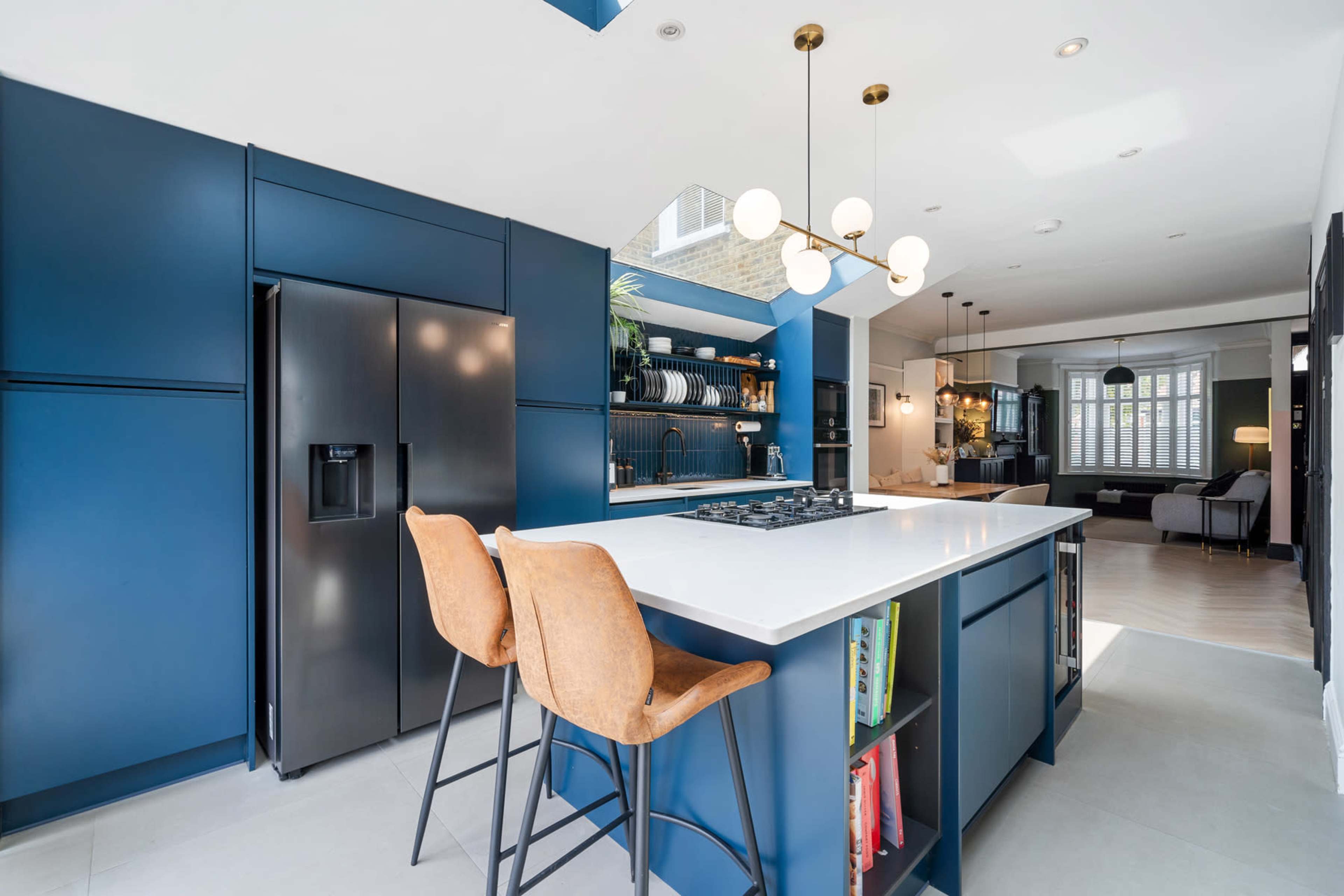 A modern kitchen features dark blue cabinetry, a white island with seating, and large windows that allow natural light to enter.