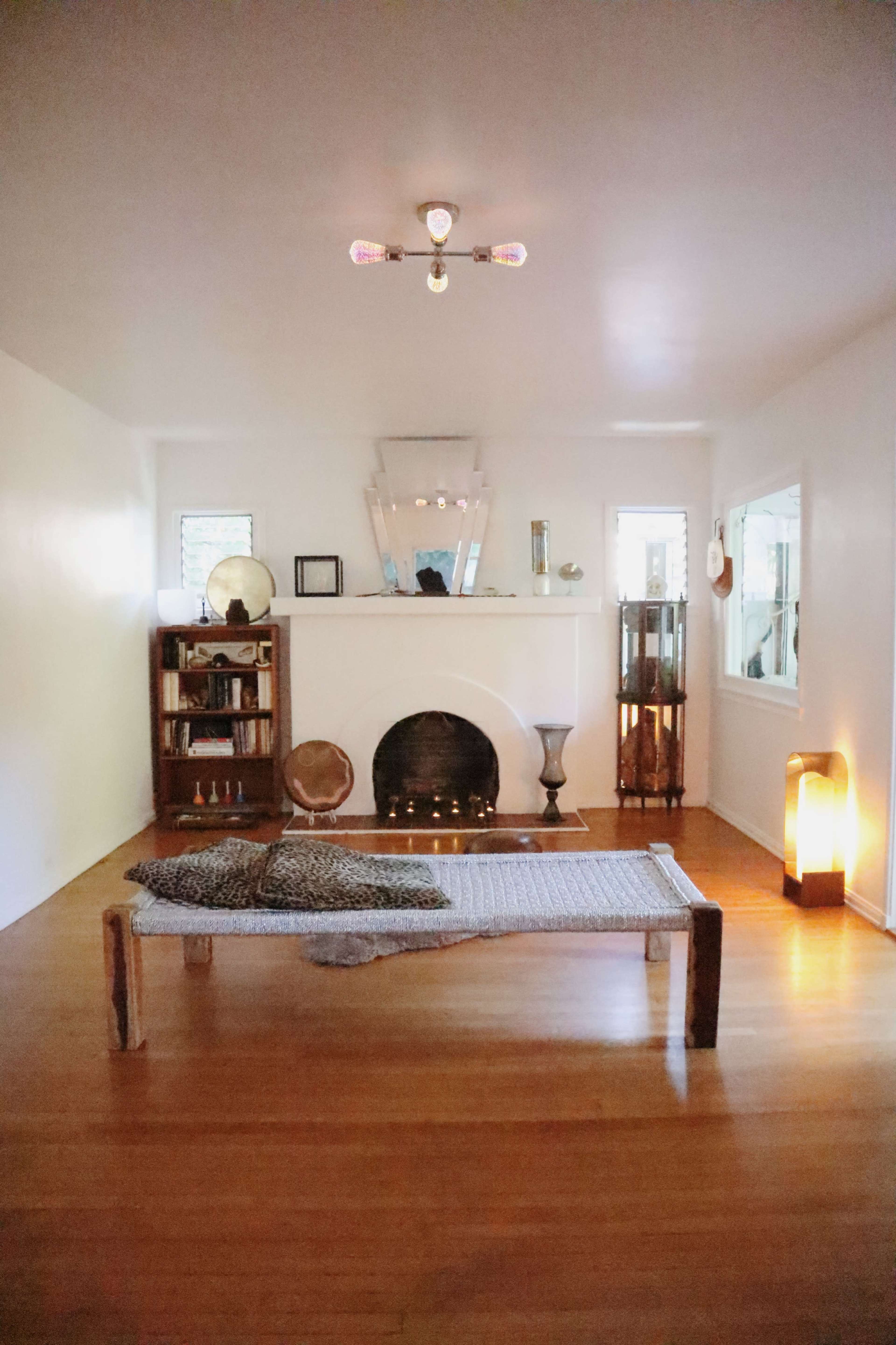 A minimalist living room featuring a wooden low bed, a fireplace, and various decorative elements on the walls and shelves.