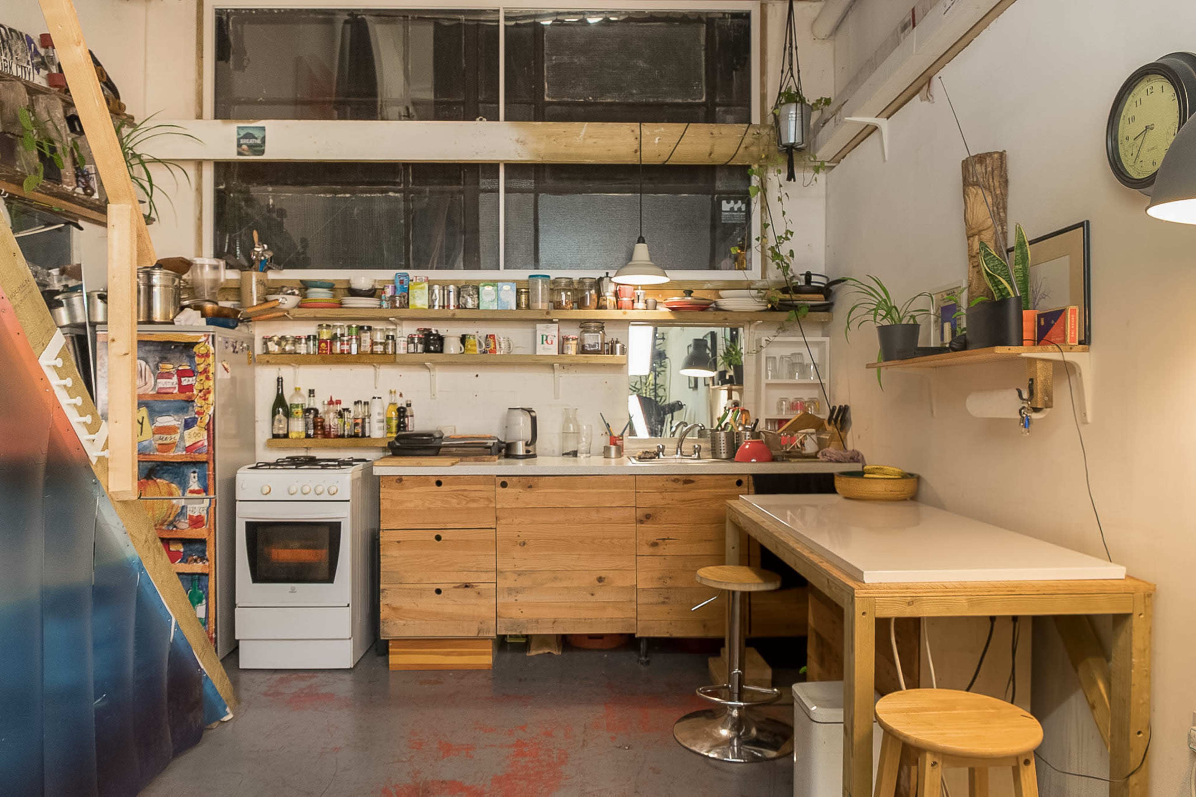 A small kitchen with wooden cabinets, a white stove, and shelves filled with various kitchen items and plants.