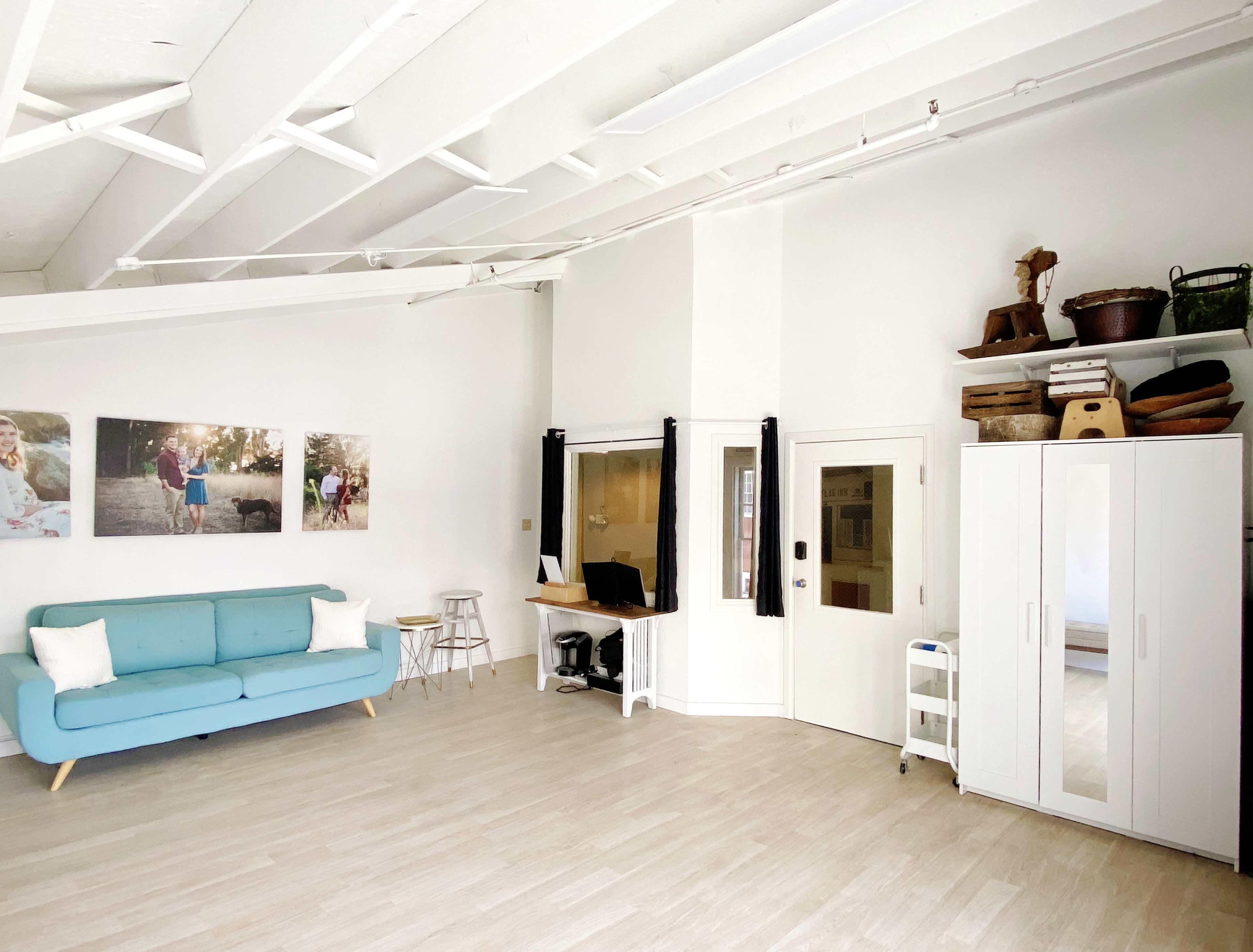 A bright, minimalist room with a light blue couch, a desk with a computer, and a white cabinet against the wall, featuring framed photographs and wooden decor items.