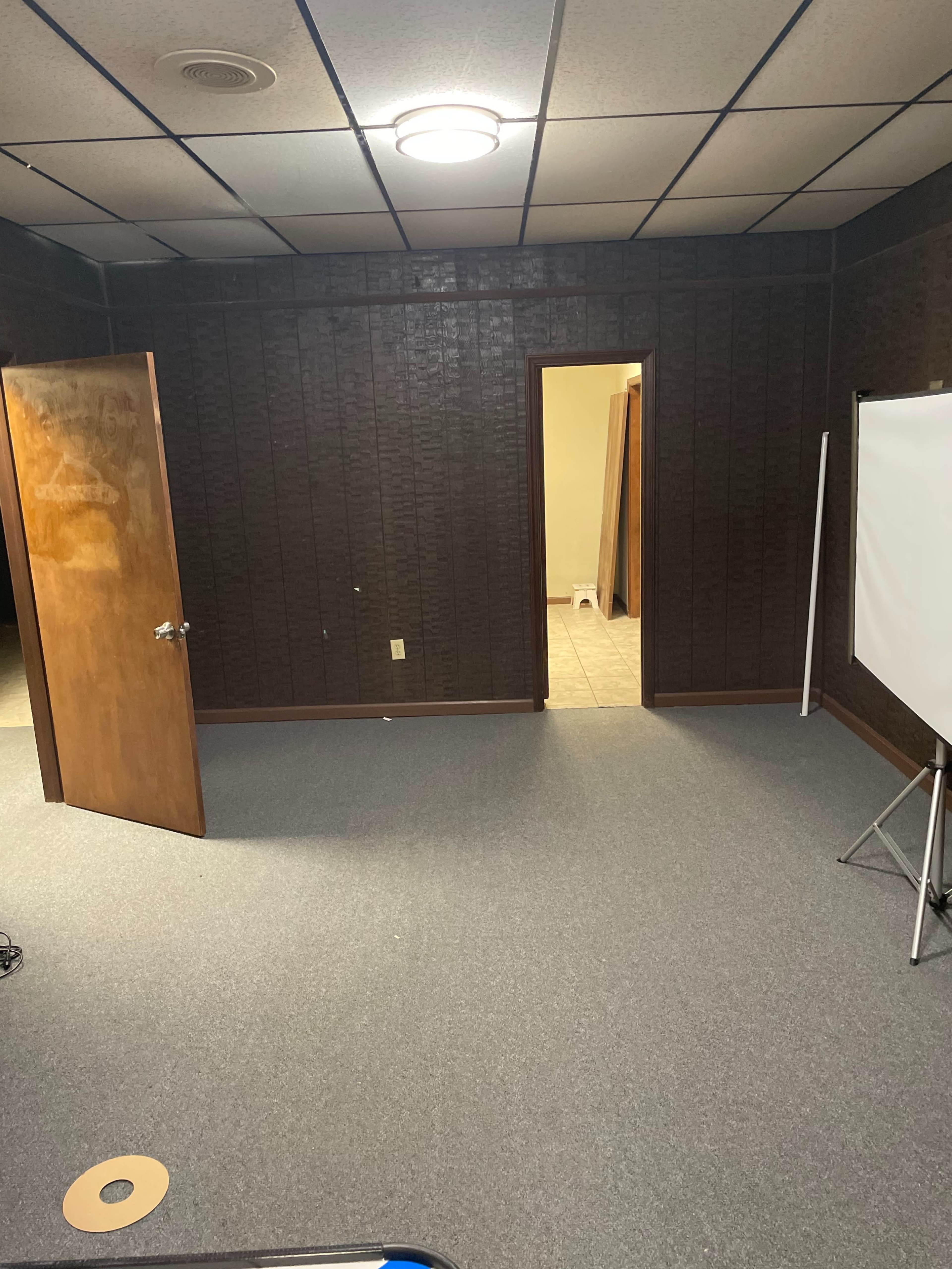 An empty room with brown walls, a door on the left, and a doorway leading to another space on the right, featuring a light-colored floor.