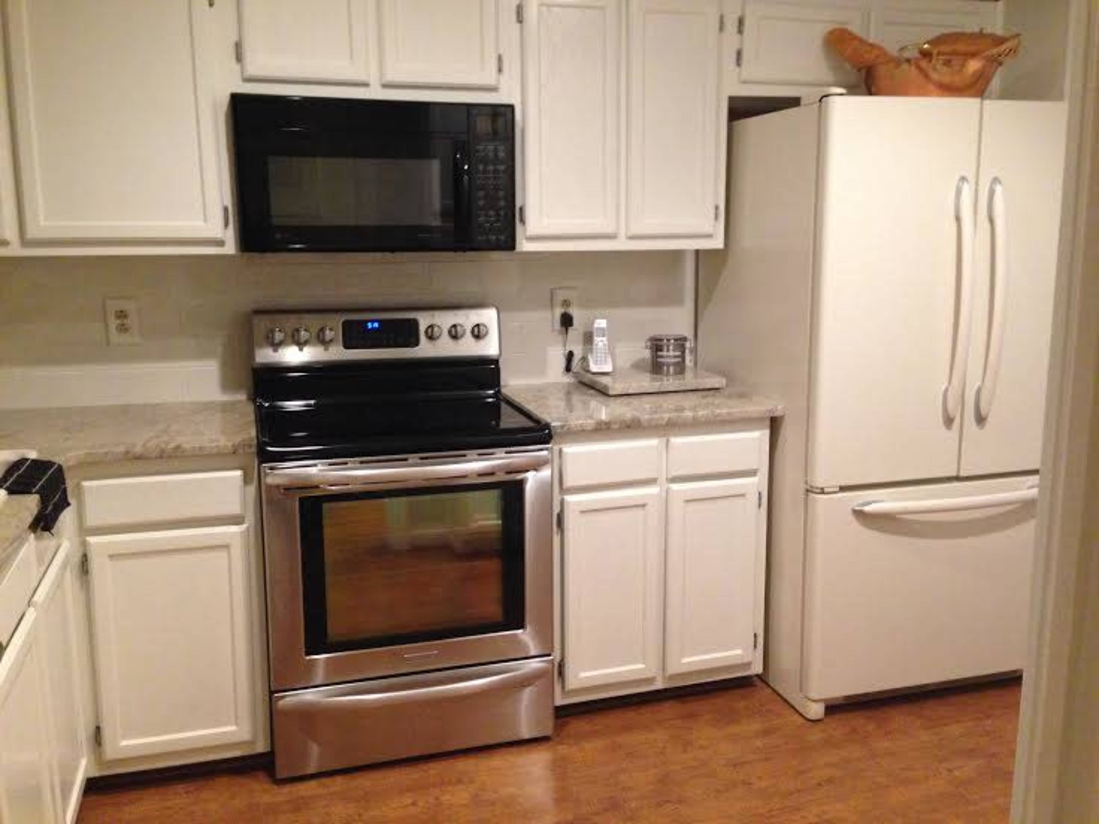 A kitchen featuring white cabinetry, a black oven and stove combination, a silver microwave, and a white refrigerator.