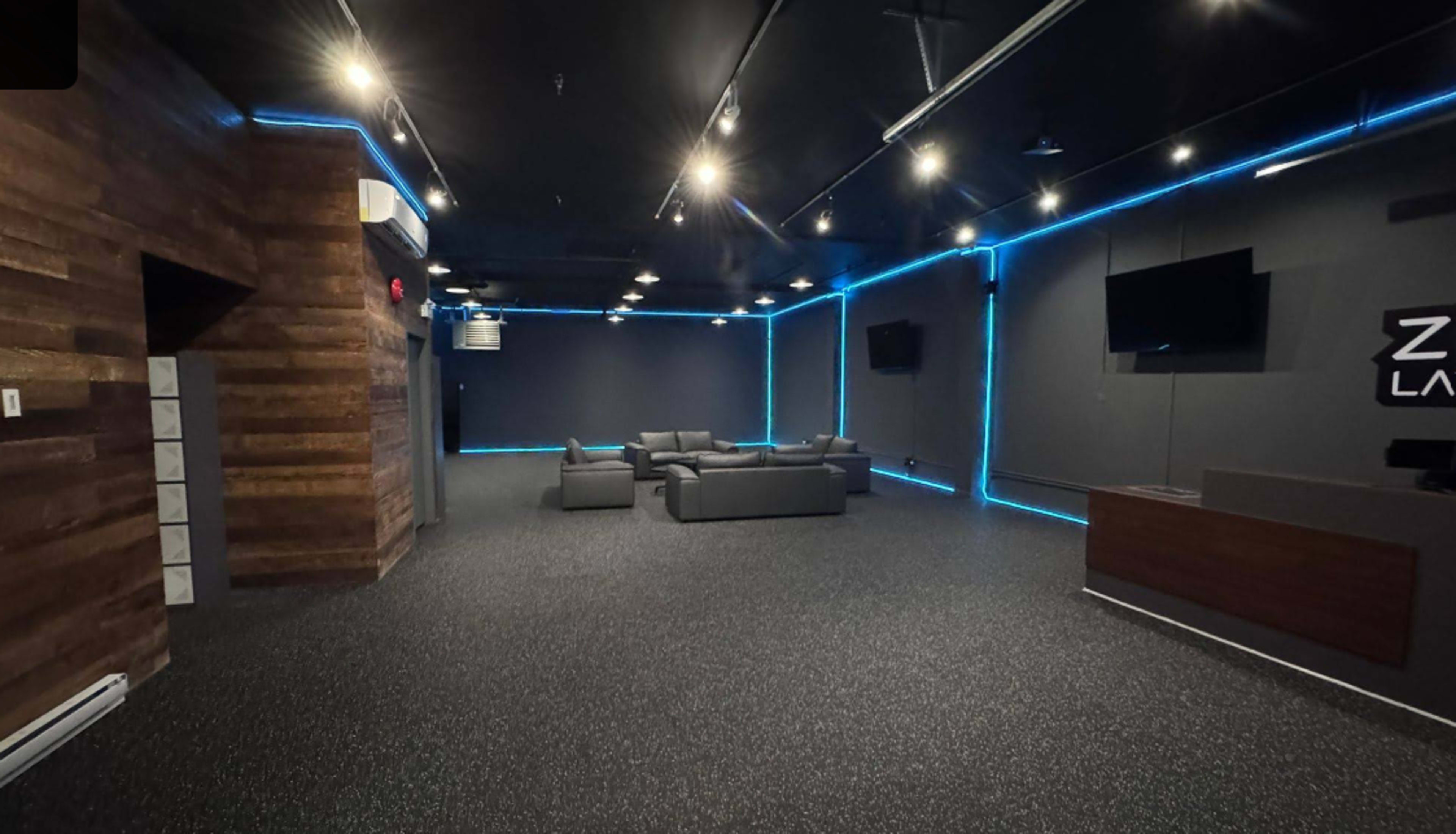 The image shows an empty room with modern seating, dark walls, blue LED lighting, and a reception area.