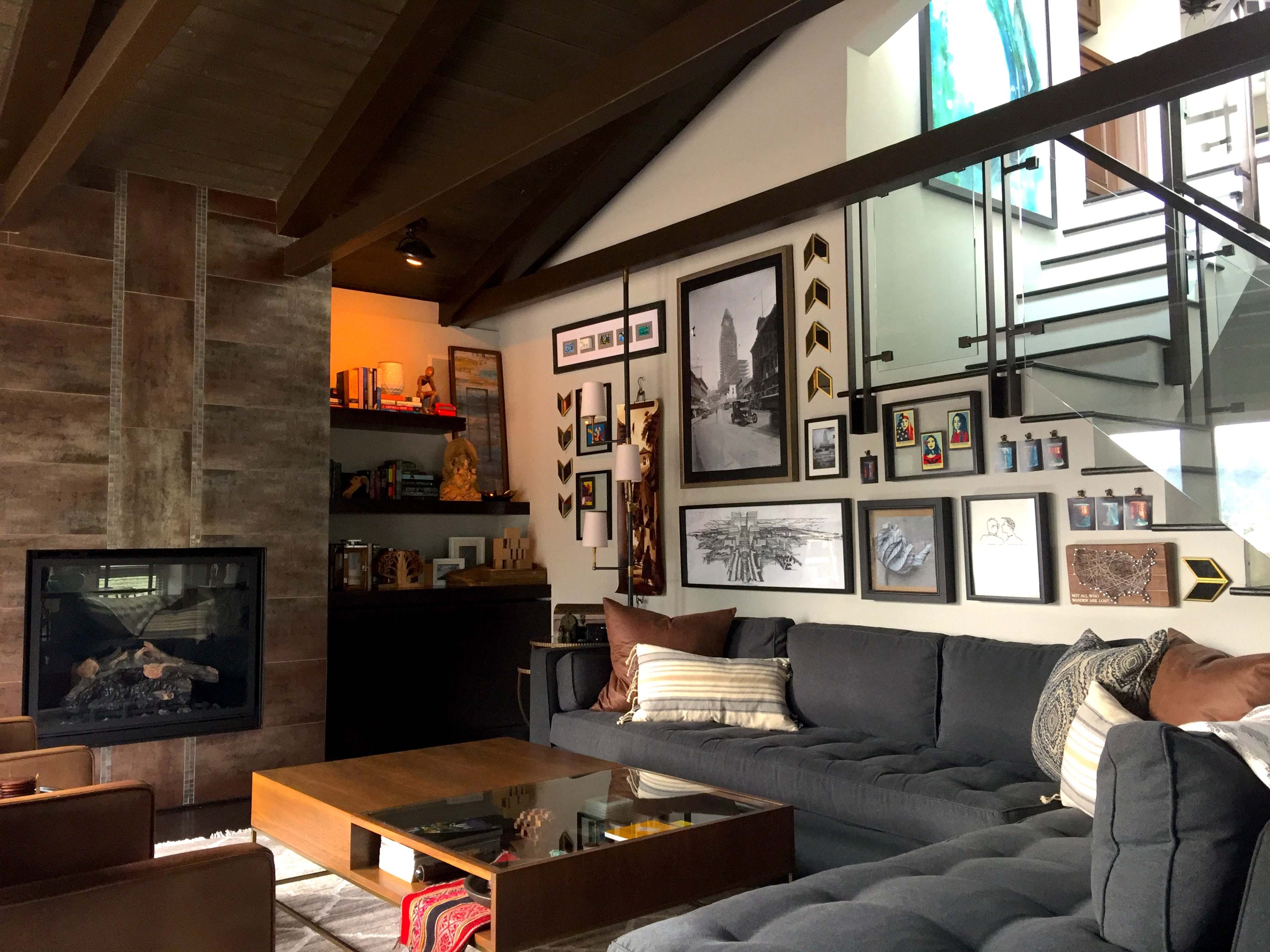 A modern living room features a sectional sofa, a coffee table, and a fireplace, with an array of framed artwork and photographs on the wall.