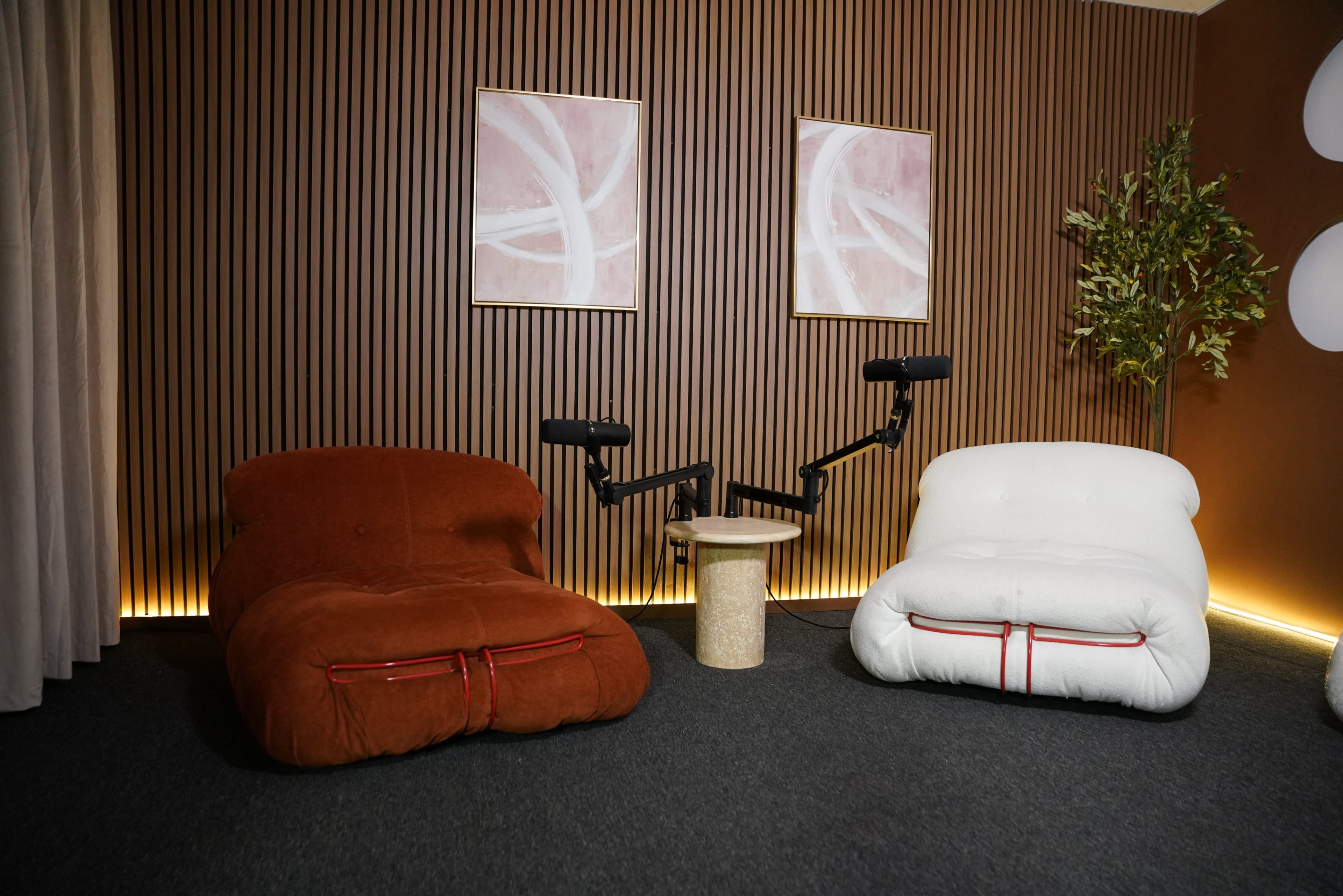 The image shows two oversized, cushioned chairs in earthy tones positioned alongside a small round table and decorative wall art.