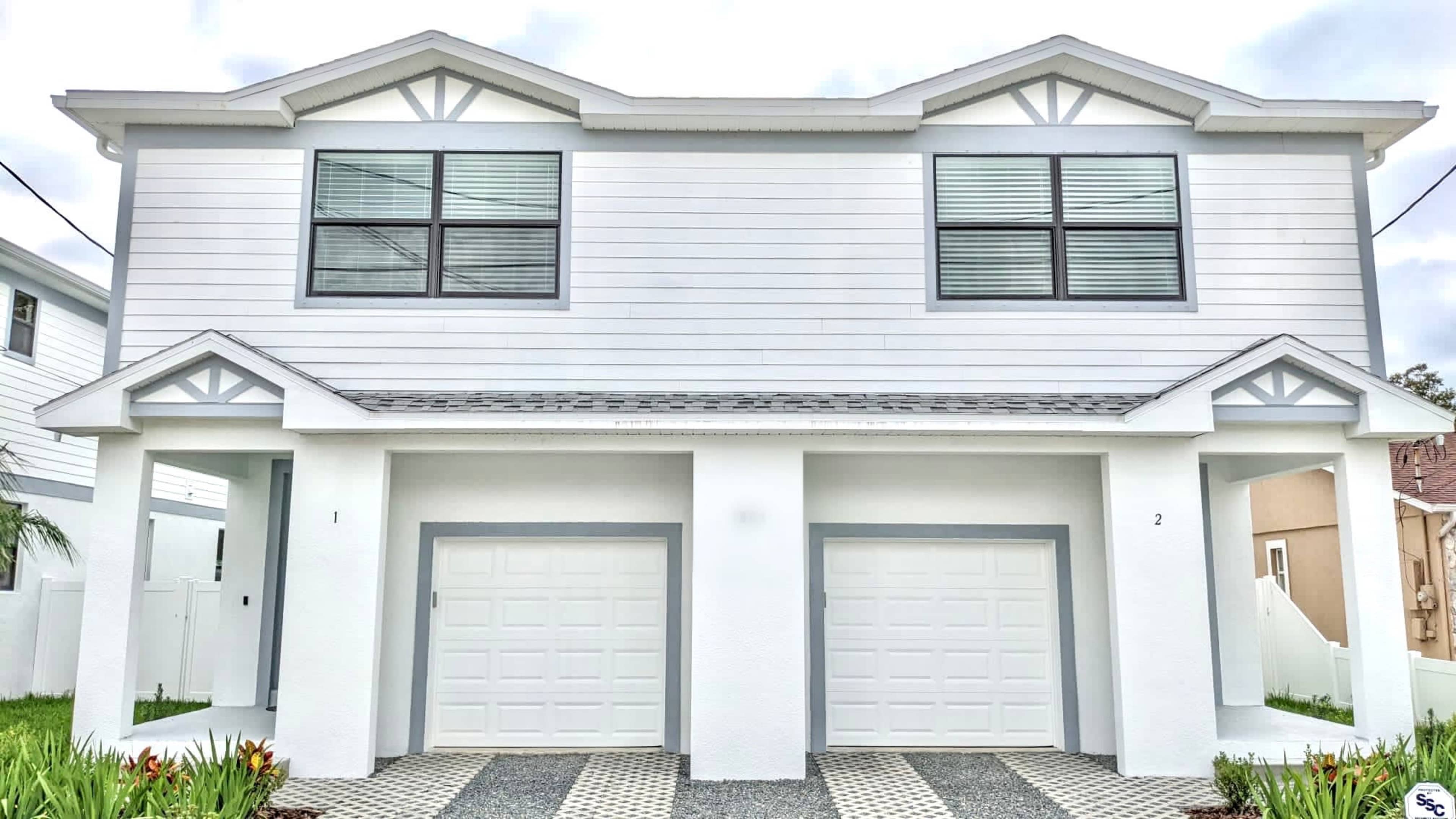 The image shows a two-story duplex with white siding and two attached garages at the front.
