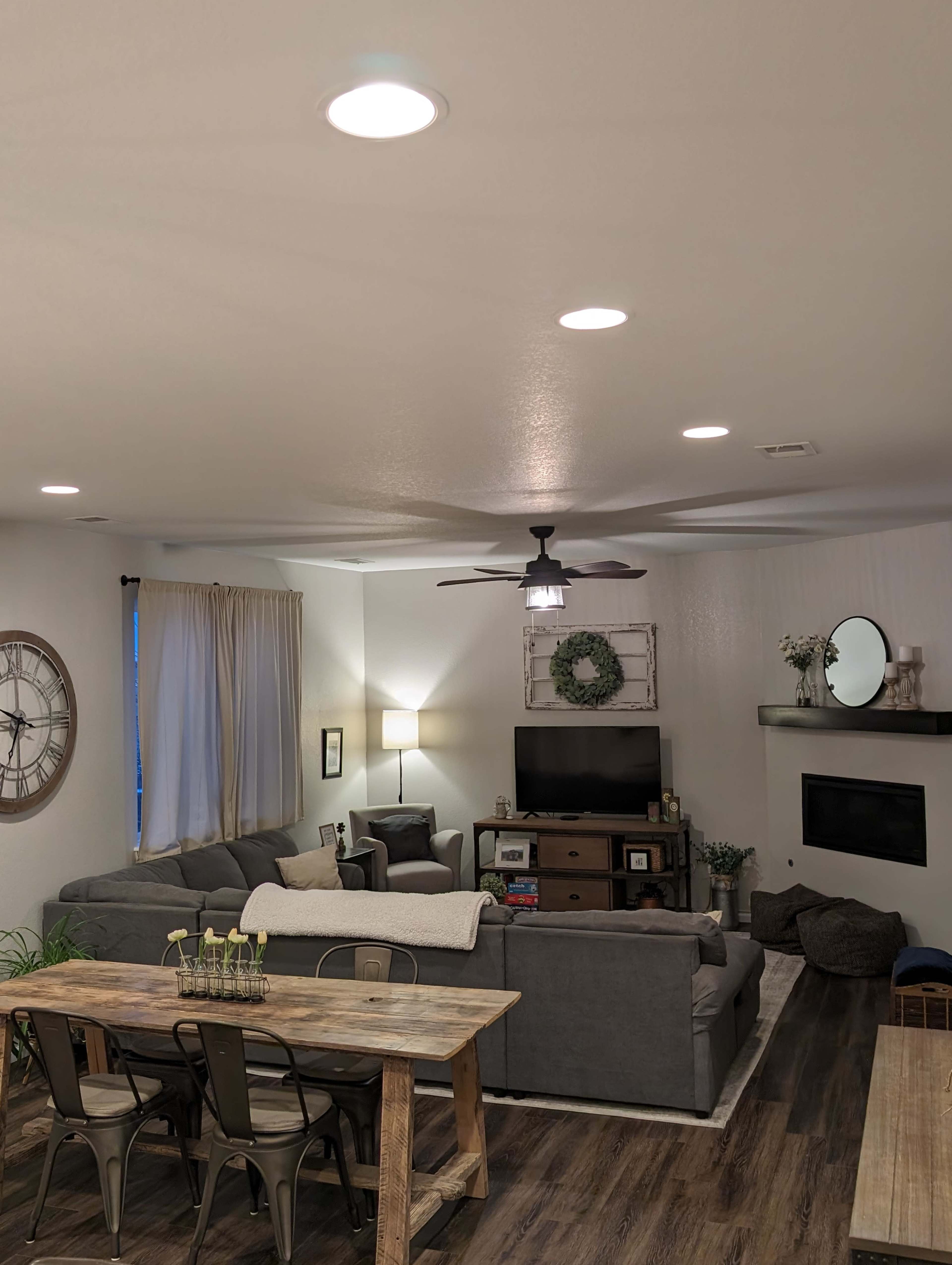 A modern living room with gray sofas, a wooden dining table, and a wall-mounted television.