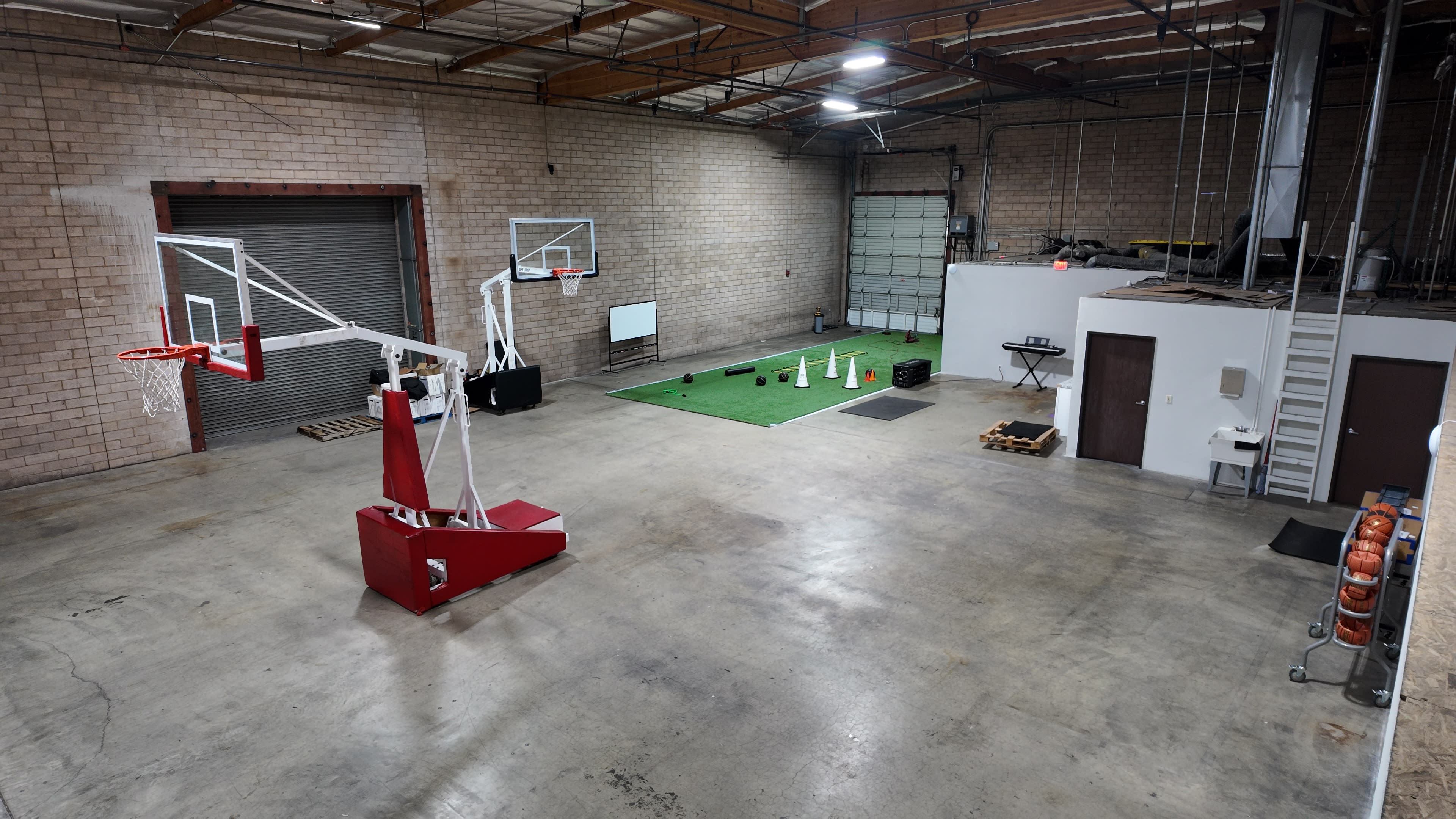 The image shows a spacious indoor area featuring a basketball hoop, a small putting green, and various sports equipment scattered on the floor.