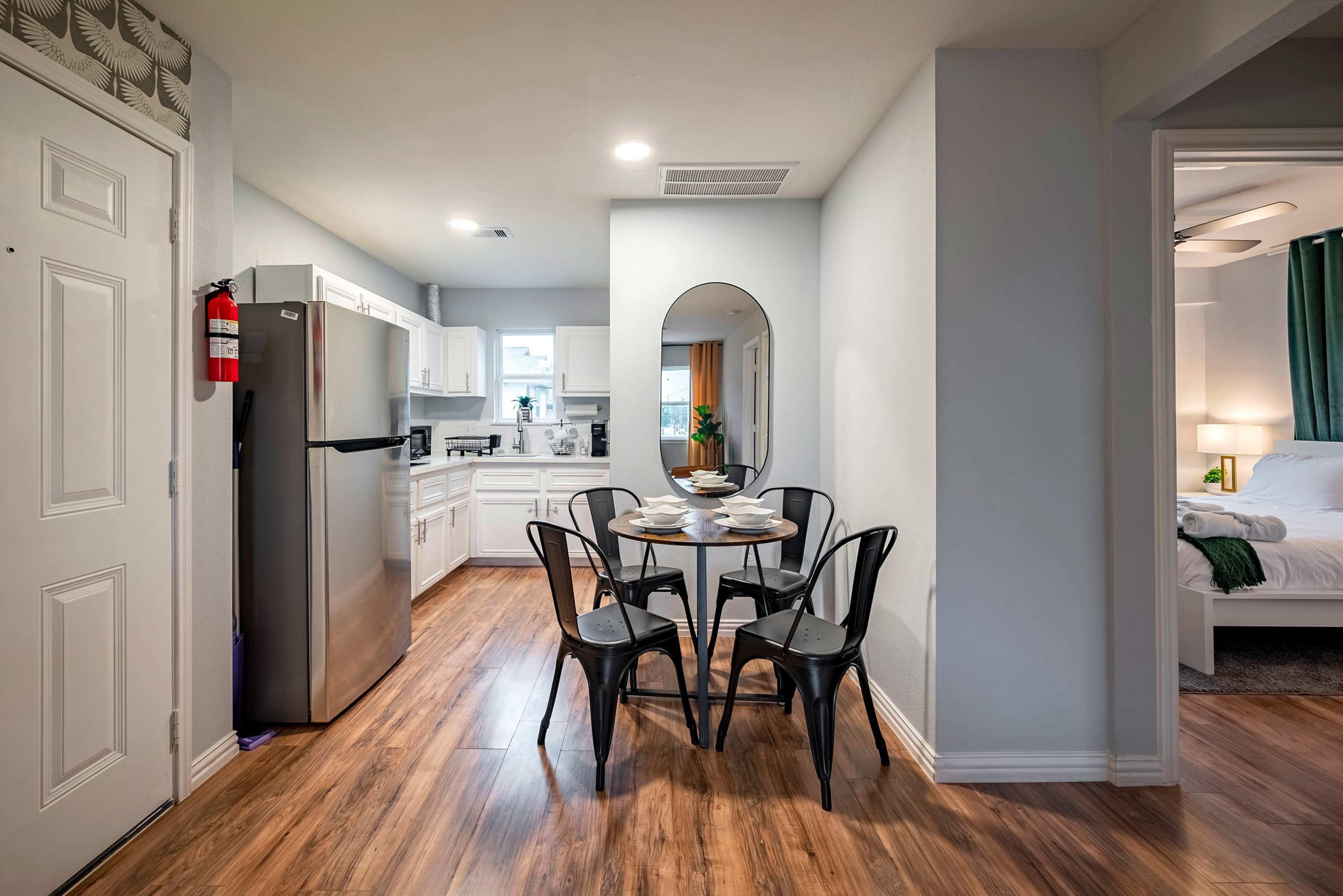 A compact dining area features a round table with four chairs, adjacent to a kitchen and leading to a bedroom.