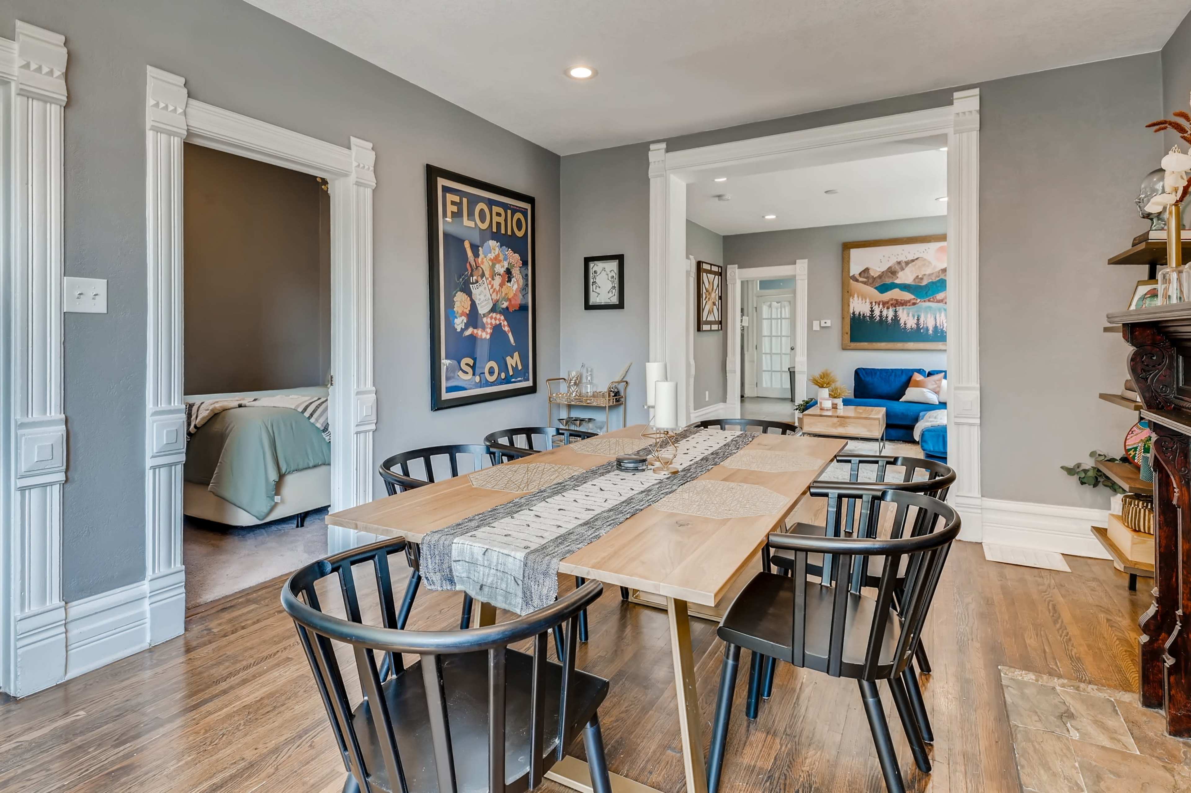 A dining area with a wooden table surrounded by black chairs, featuring artwork on the walls and an adjoining living space.