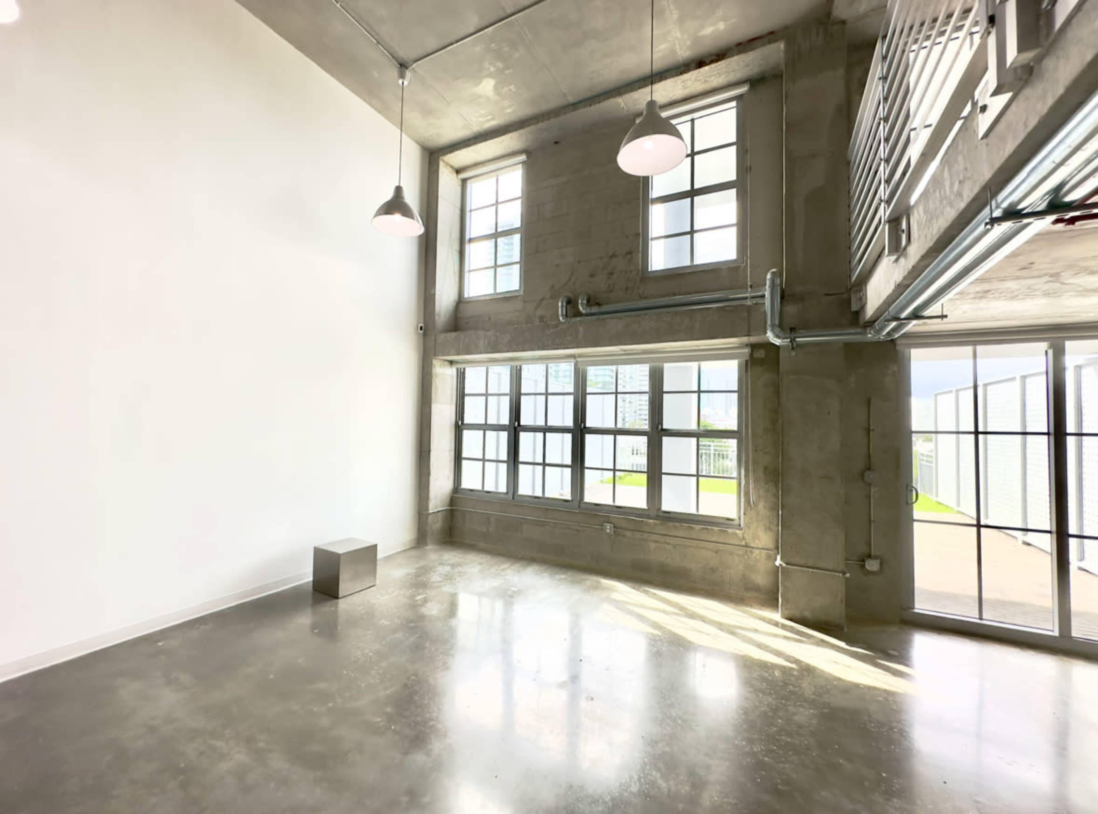 A modern, minimalist room with large windows, polished concrete floors, and overhead lighting.