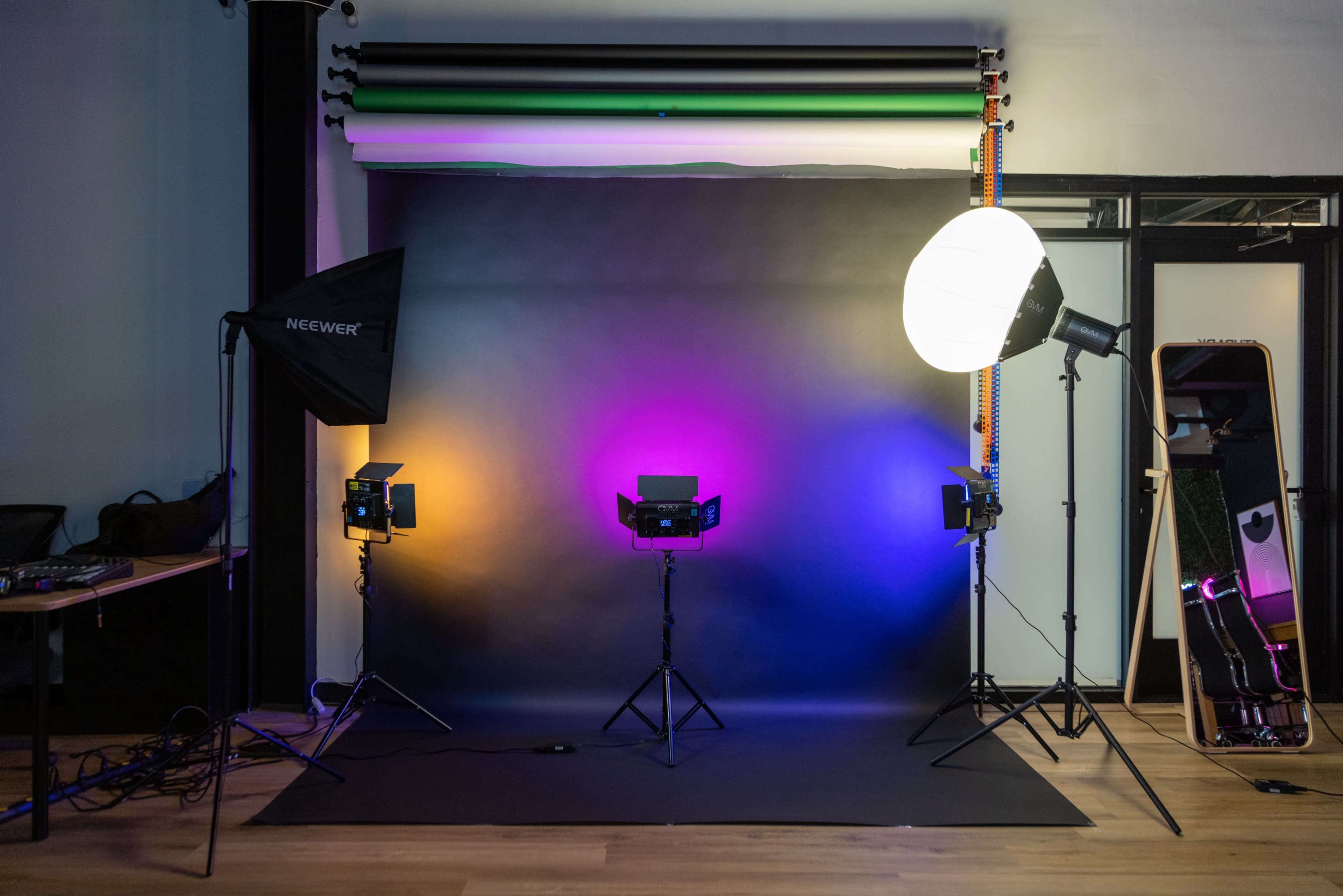 The image shows a photography studio setup with three lights on stands, a backdrop, and a mirror.