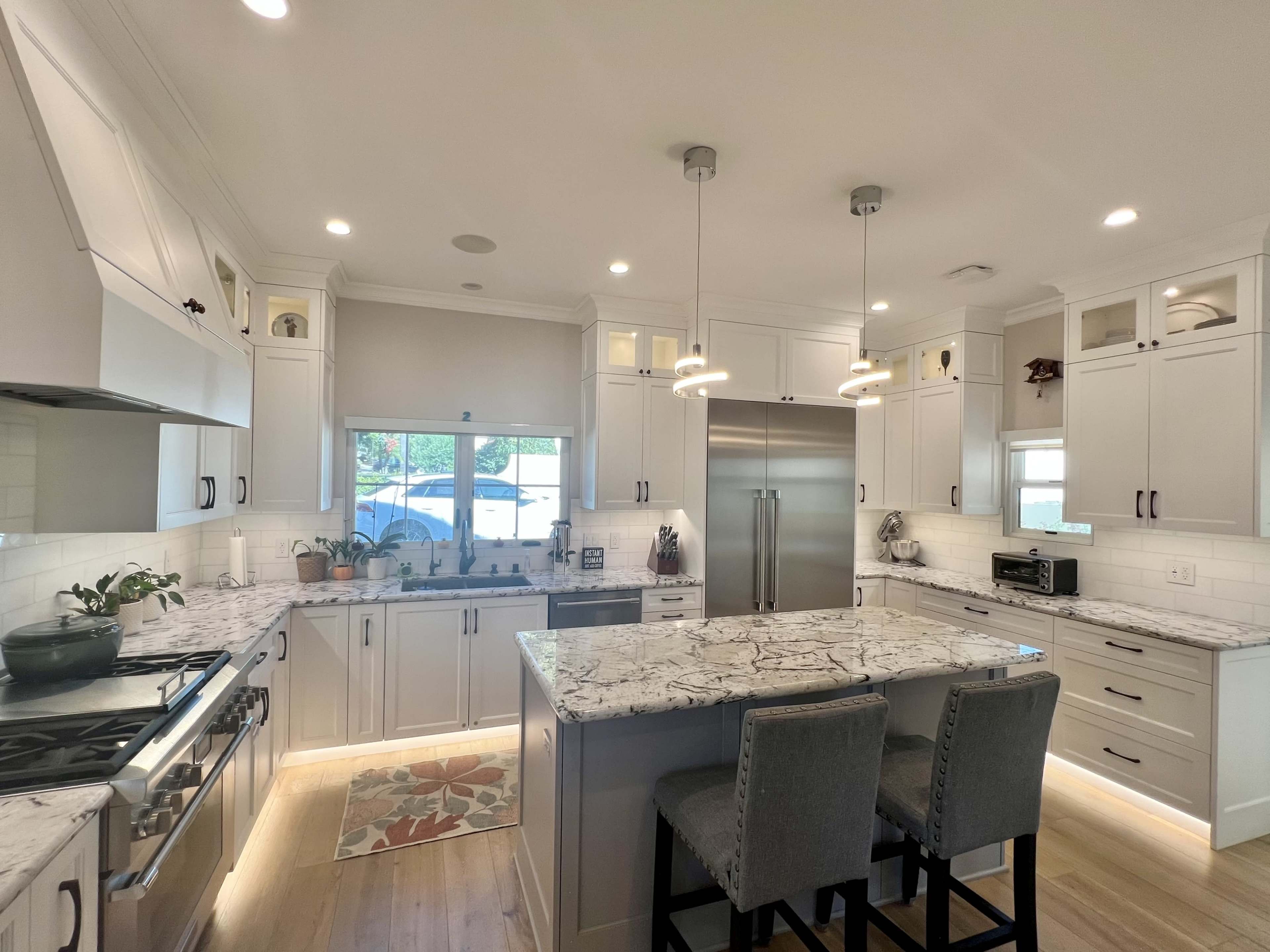 A modern kitchen featuring white cabinets, a large island with a marble countertop, and stainless steel appliances.
