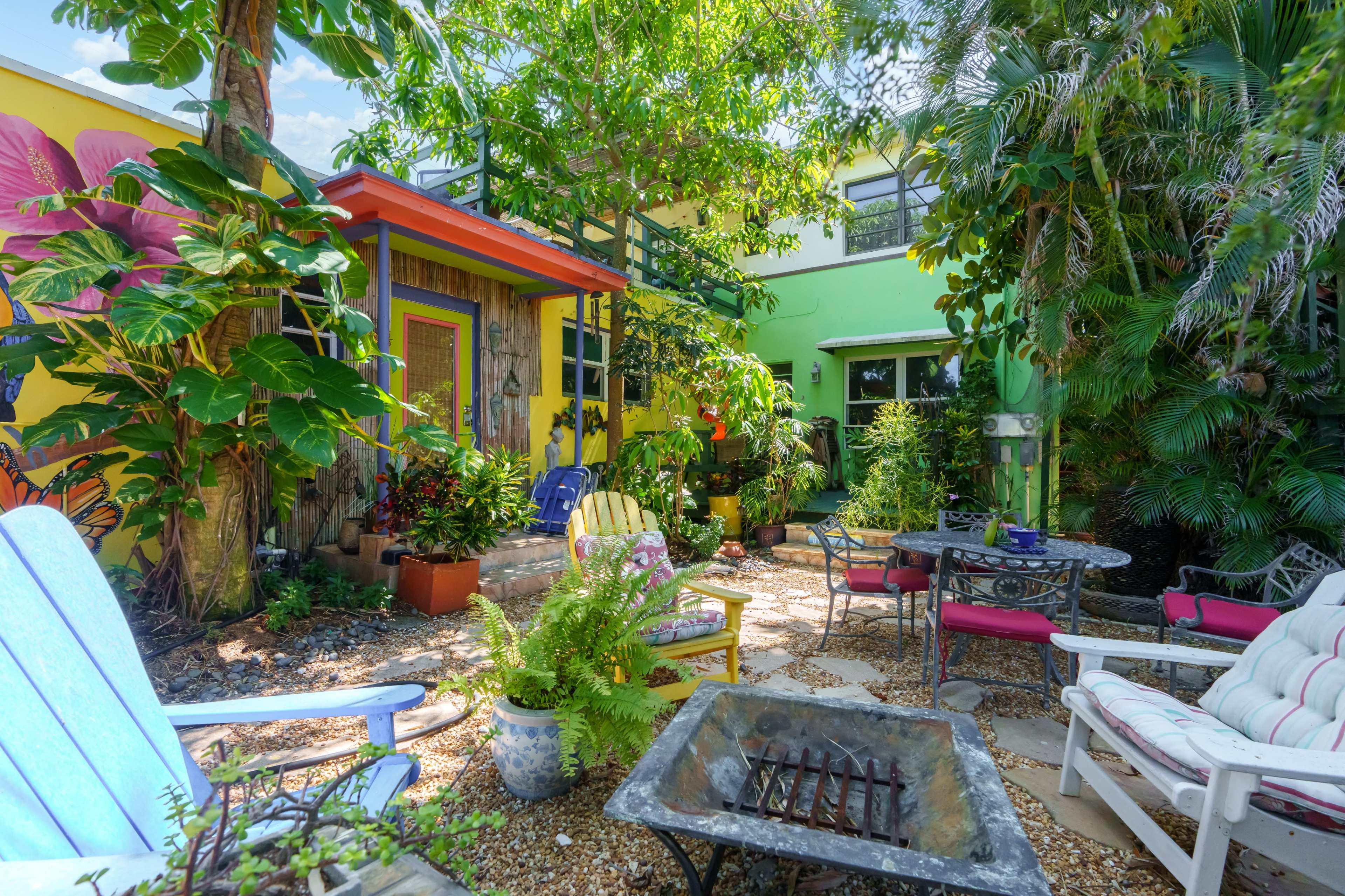 A colorful garden patio features various plants, outdoor furniture, and a fire pit surrounded by brightly painted walls.