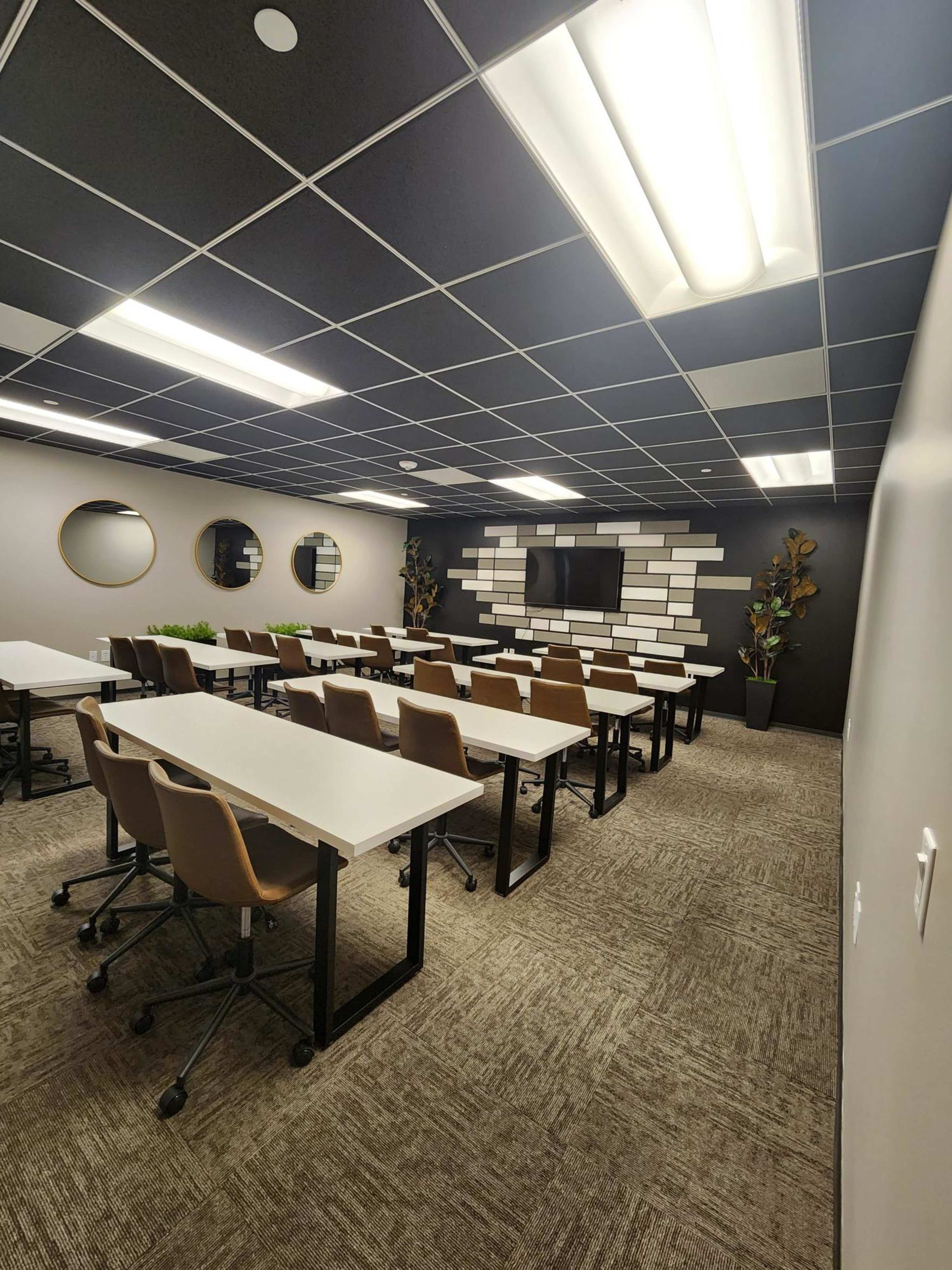 The image shows a modern classroom setup with multiple rows of white tables and brown chairs, featuring a wall mounted screen and decorative elements.