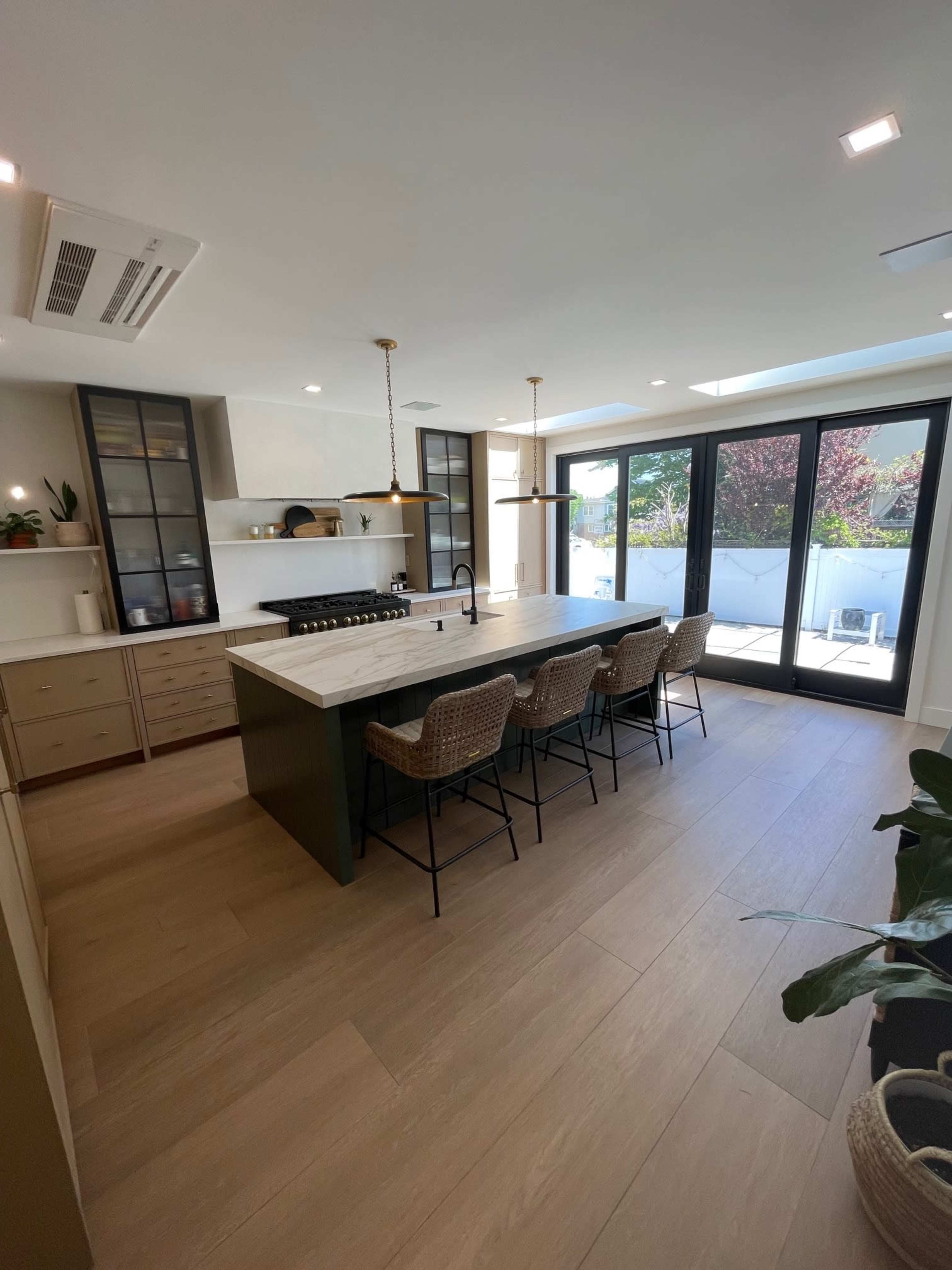 A modern kitchen features a large island with a marble countertop, seating for six, and sliding glass doors leading to an outdoor area.