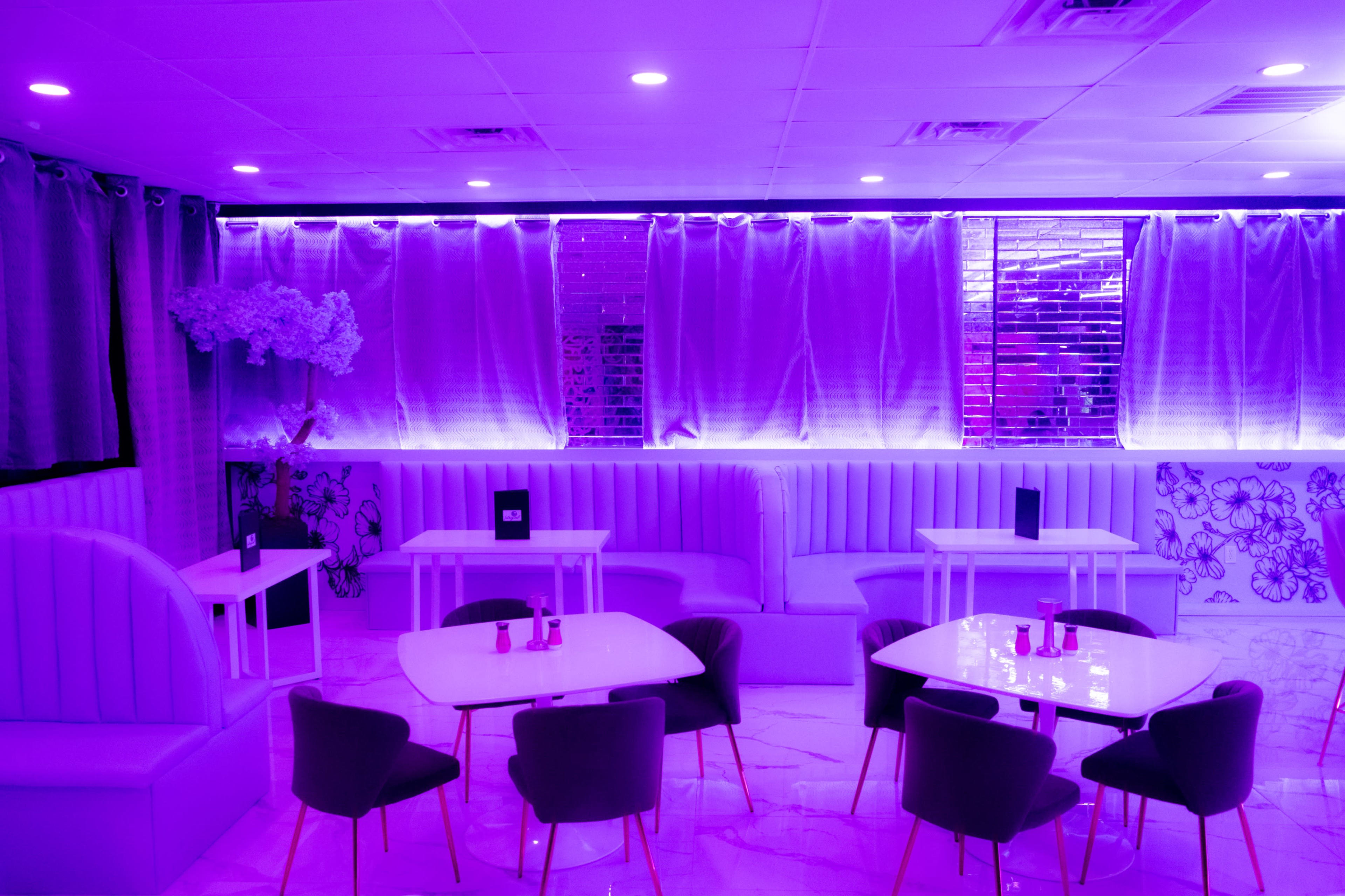 The scene features a modern lounge with purple lighting, upholstered seating, and white tables arranged around the space.