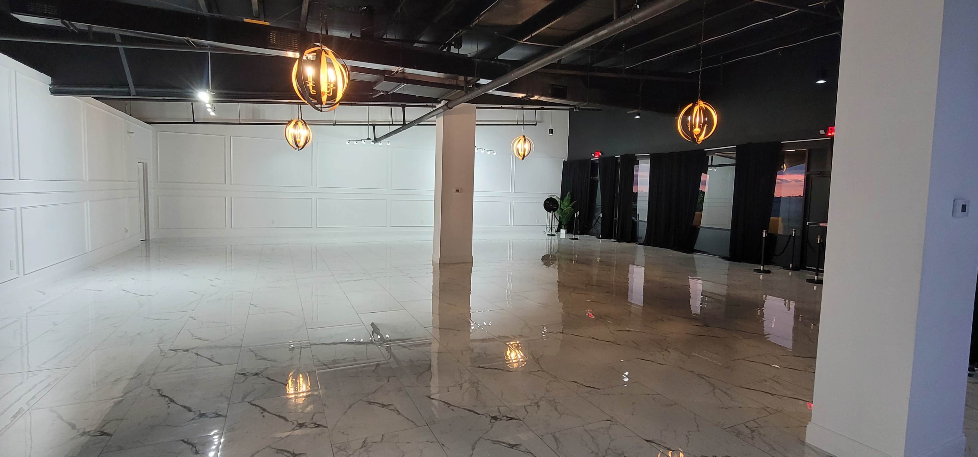 A spacious, empty room with polished marble floors, white walls, and pendant light fixtures.