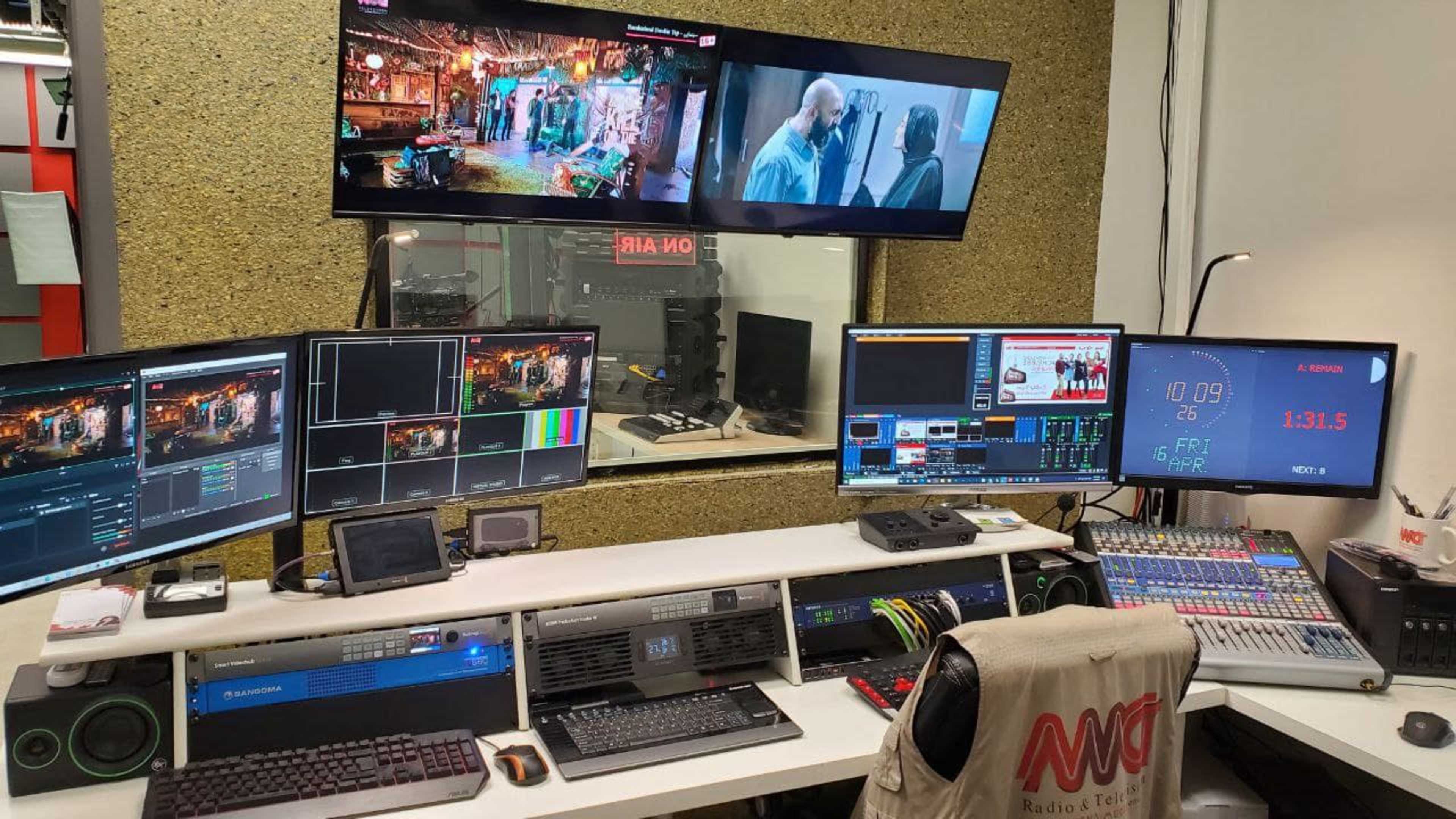 A radio and television broadcasting studio equipped with multiple monitors, a video switcher, and a digital audio mixer.