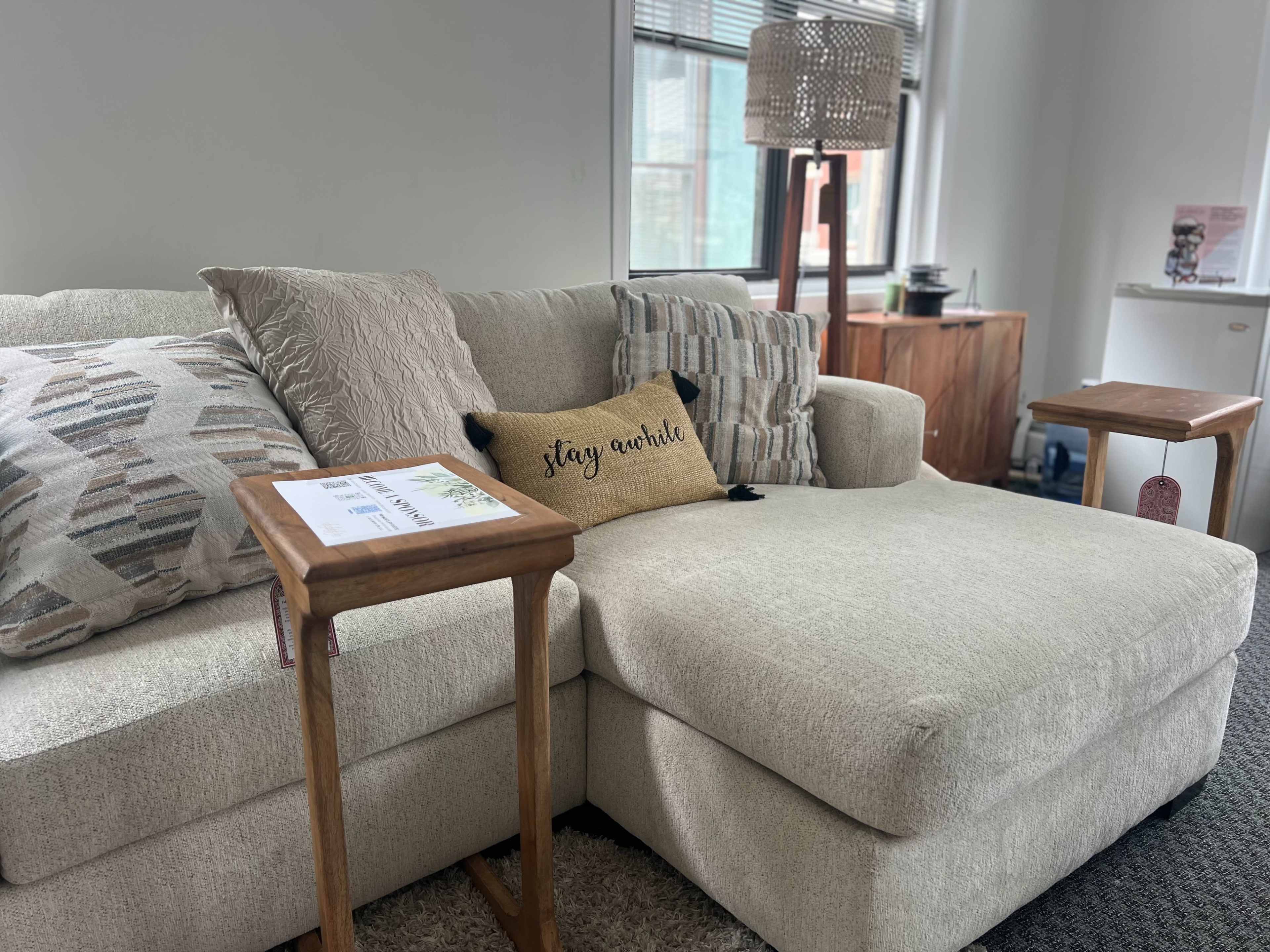 A light-colored sectional couch adorned with decorative pillows, accompanied by two small side tables in a well-lit room.