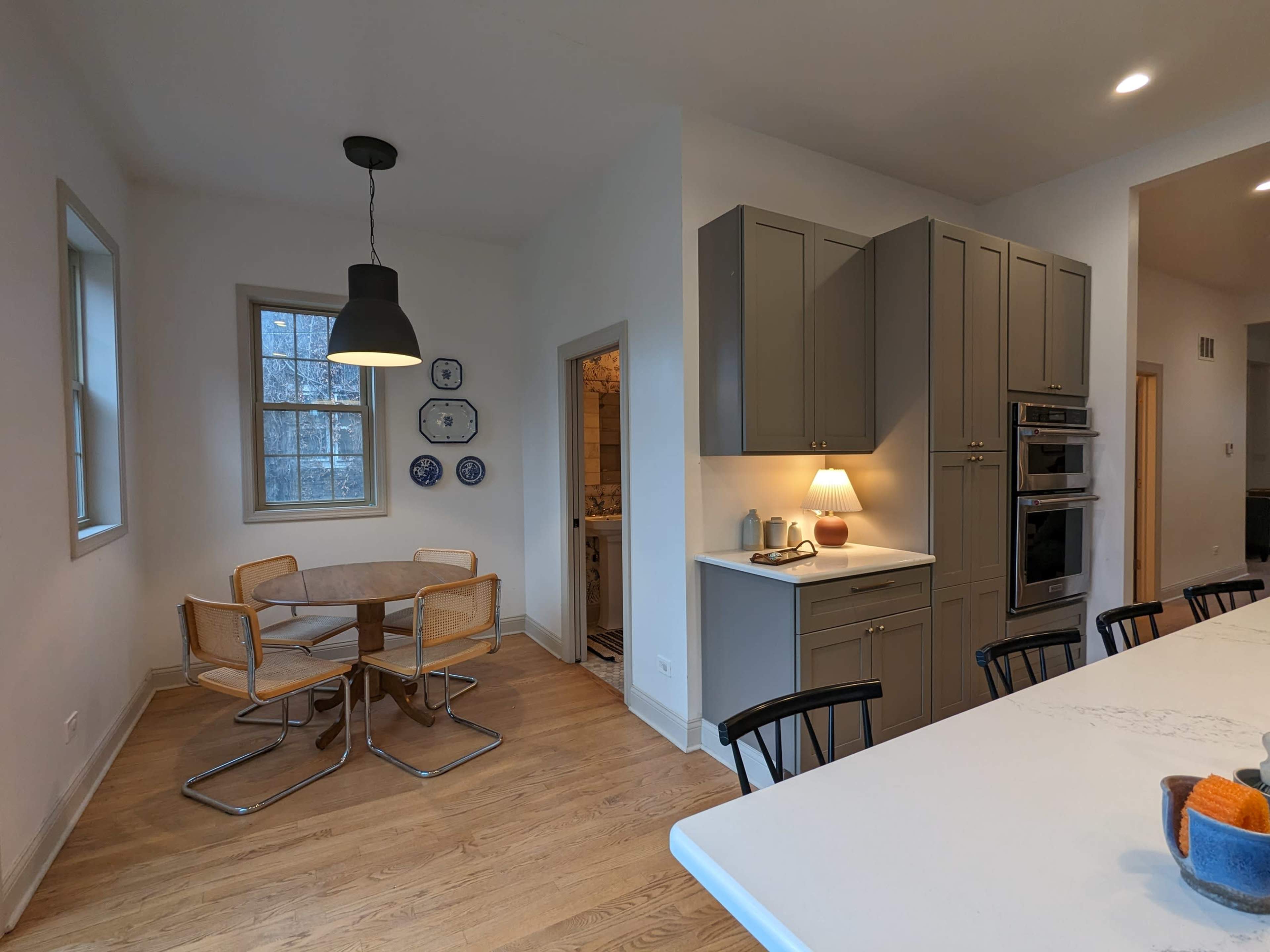 A modern kitchen with a dining area featuring a circular table and four chairs, light cabinetry, and stainless steel appliances.