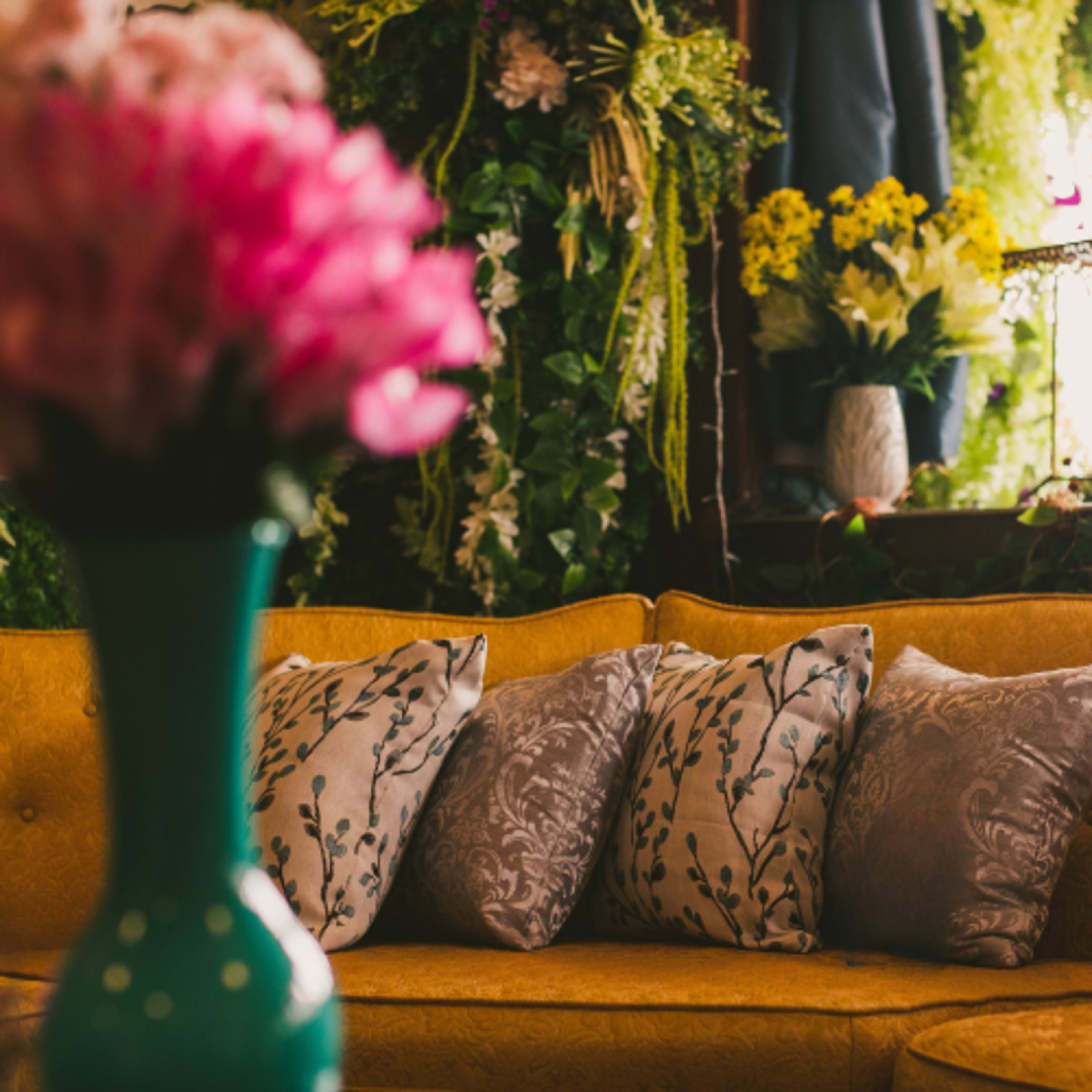 A yellow sofa with patterned pillows is surrounded by floral decor in a well-lit indoor space.