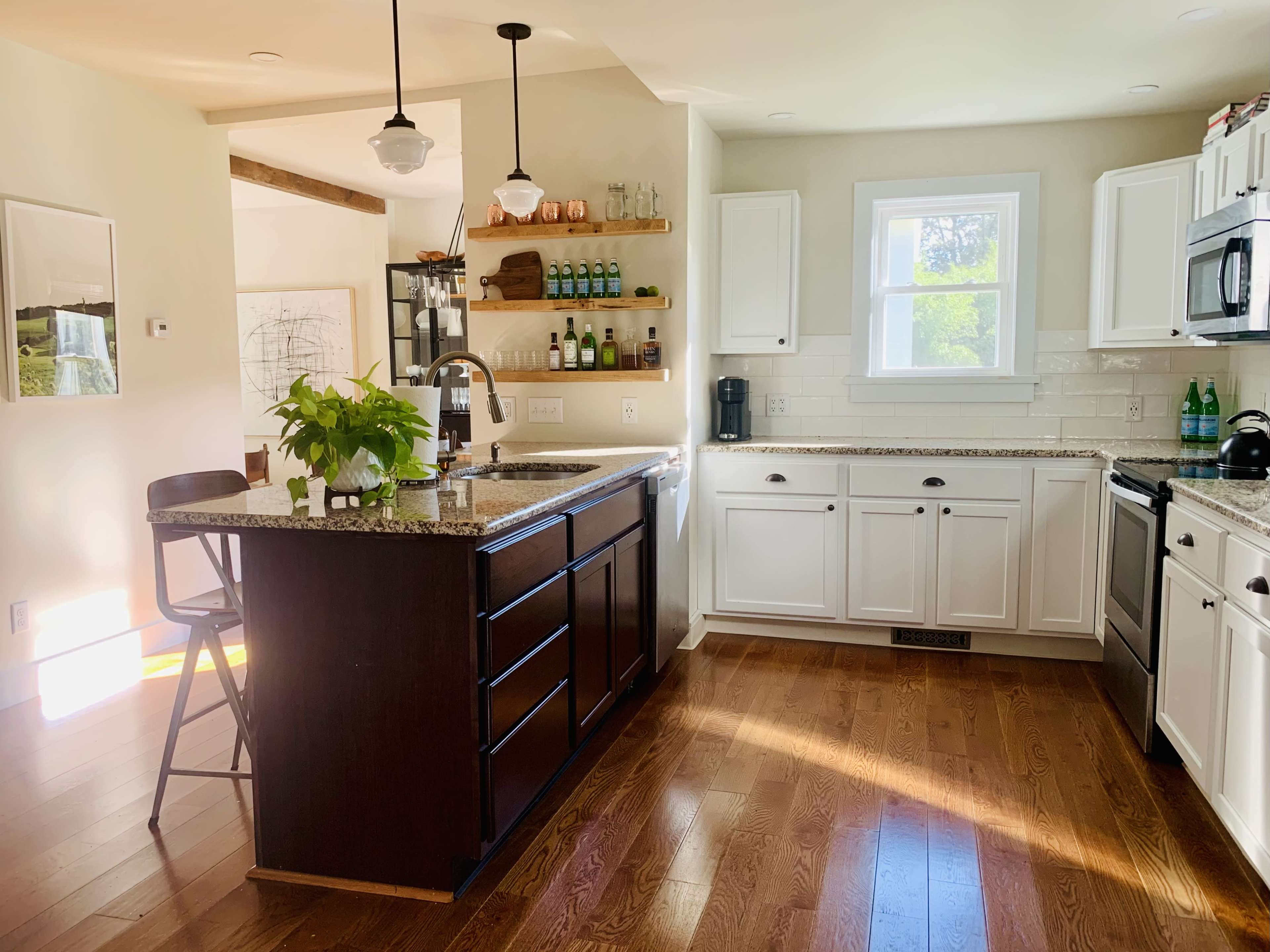 A modern kitchen features white cabinetry, a granite-topped island with seating, and natural light streaming through a window.
