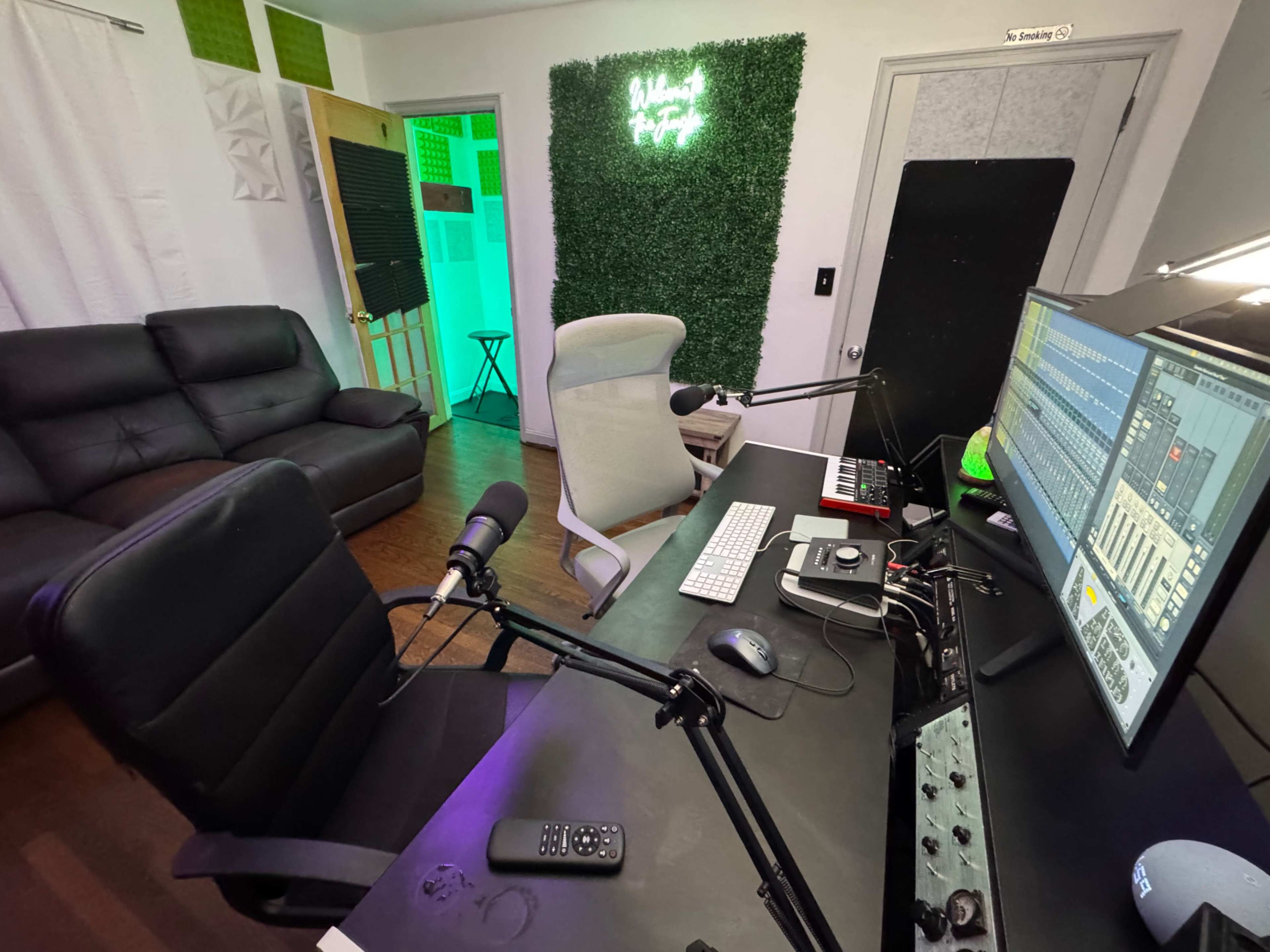 The image shows a home studio setup with a desk featuring a computer, mixer, and microphone, along with a black couch and green accent wall.