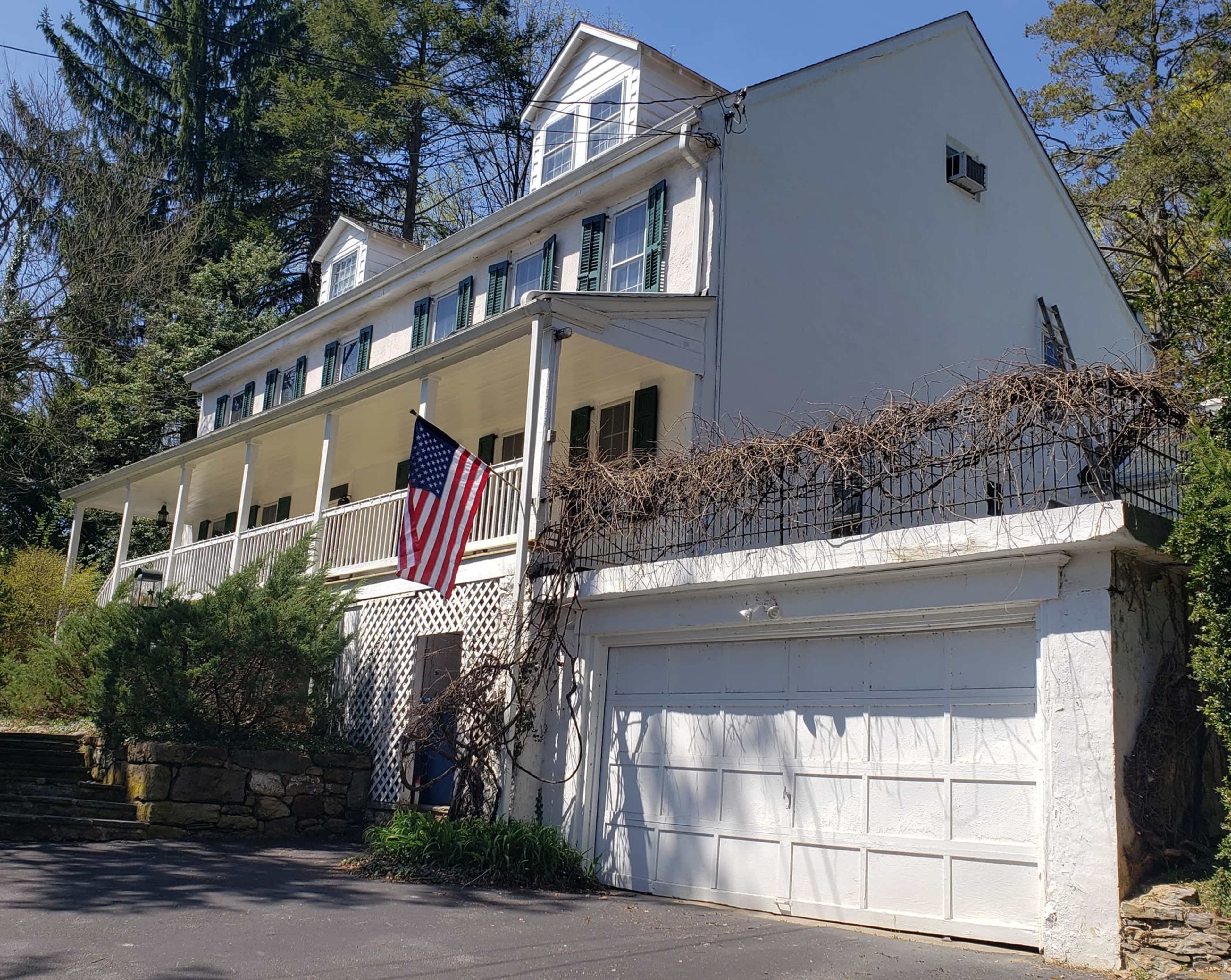 A three-story white house with a front porch, an American flag hanging, and a two-car garage.