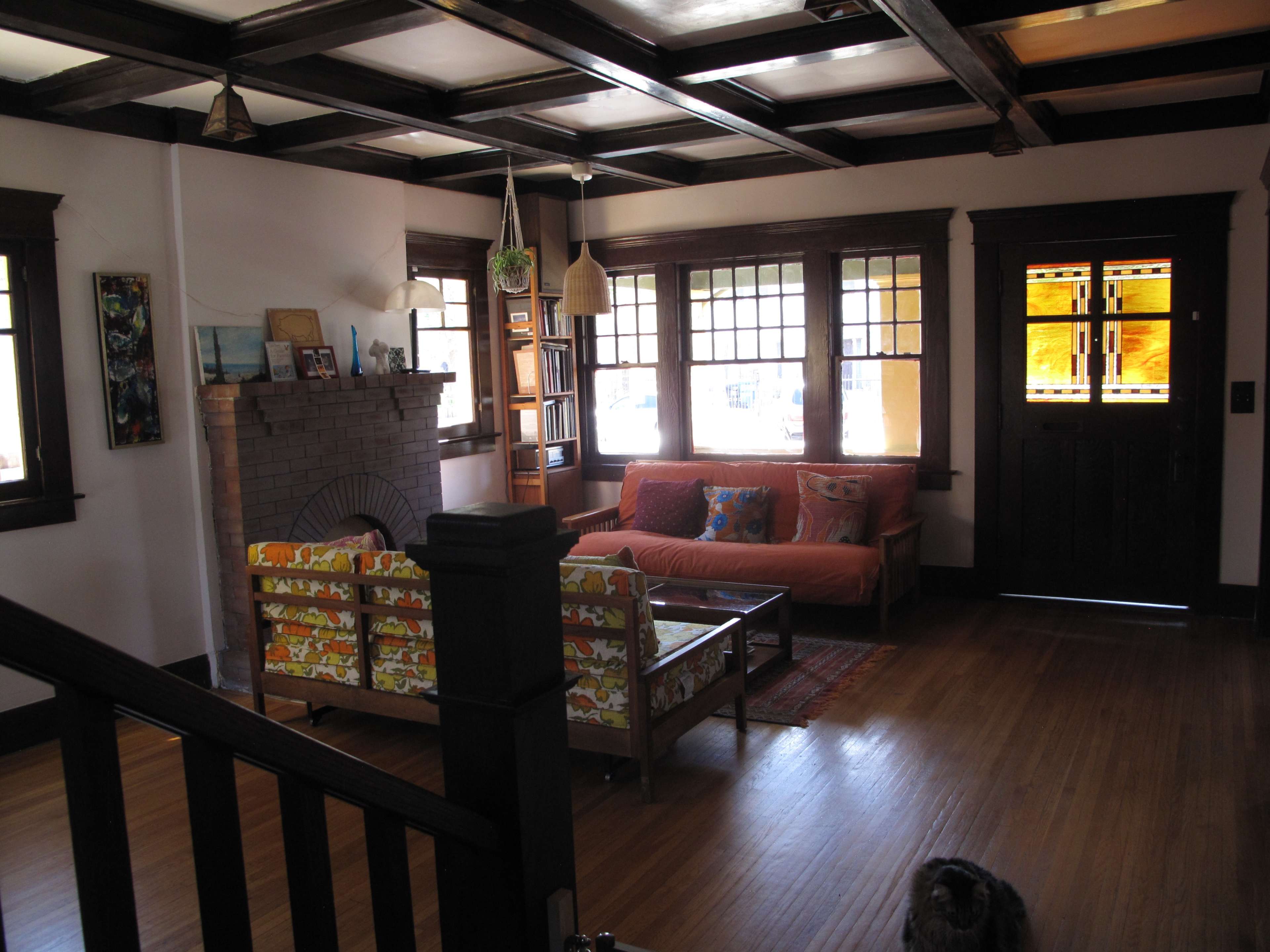 A living room featuring a brick fireplace, a patterned sofa, and a door with stained glass windows.