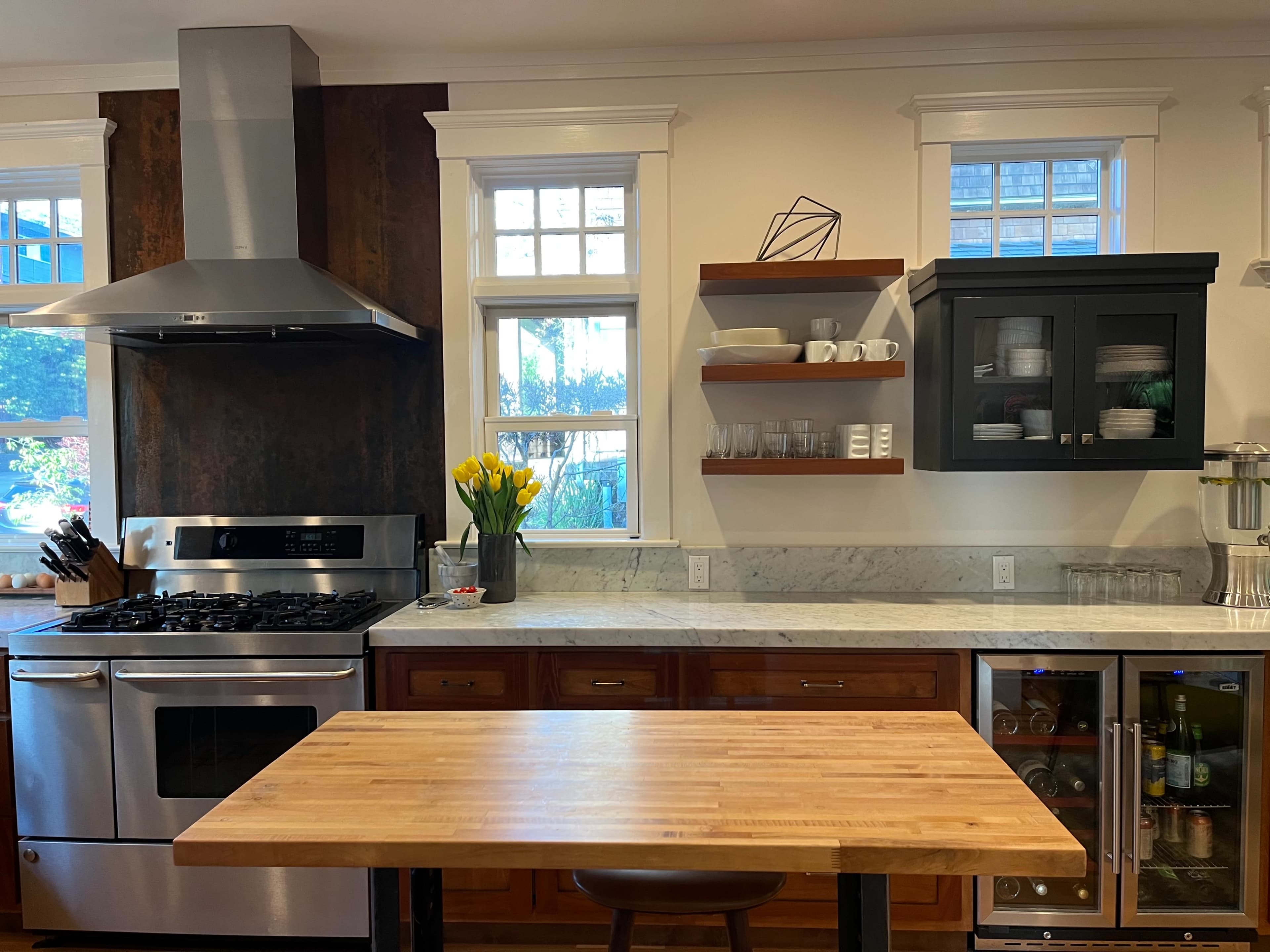 A modern kitchen features stainless steel appliances, a wooden countertop, and organized shelves displaying dishes and glassware.