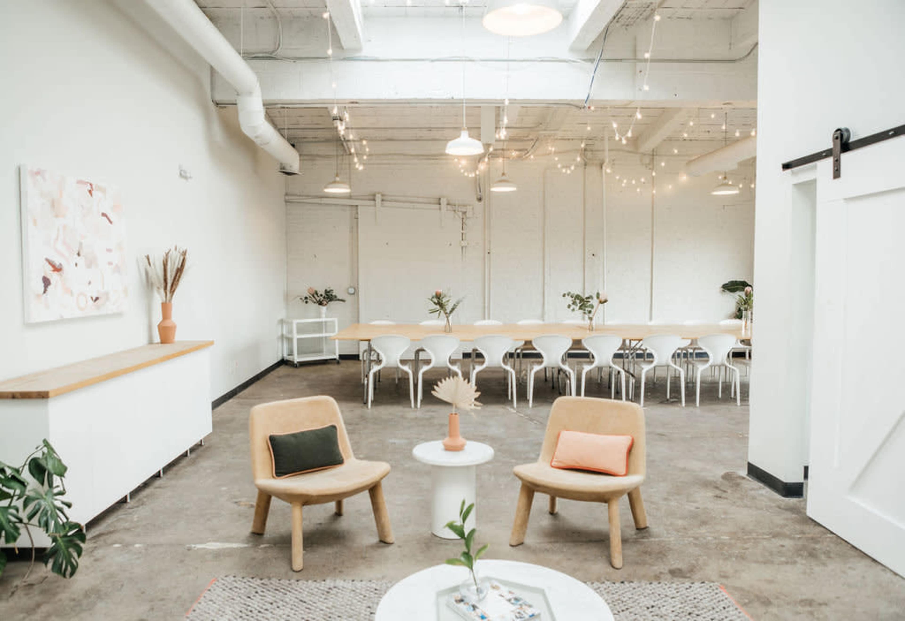The image shows a spacious, modern interior featuring two chairs in the foreground and a long dining table with white chairs in the background.