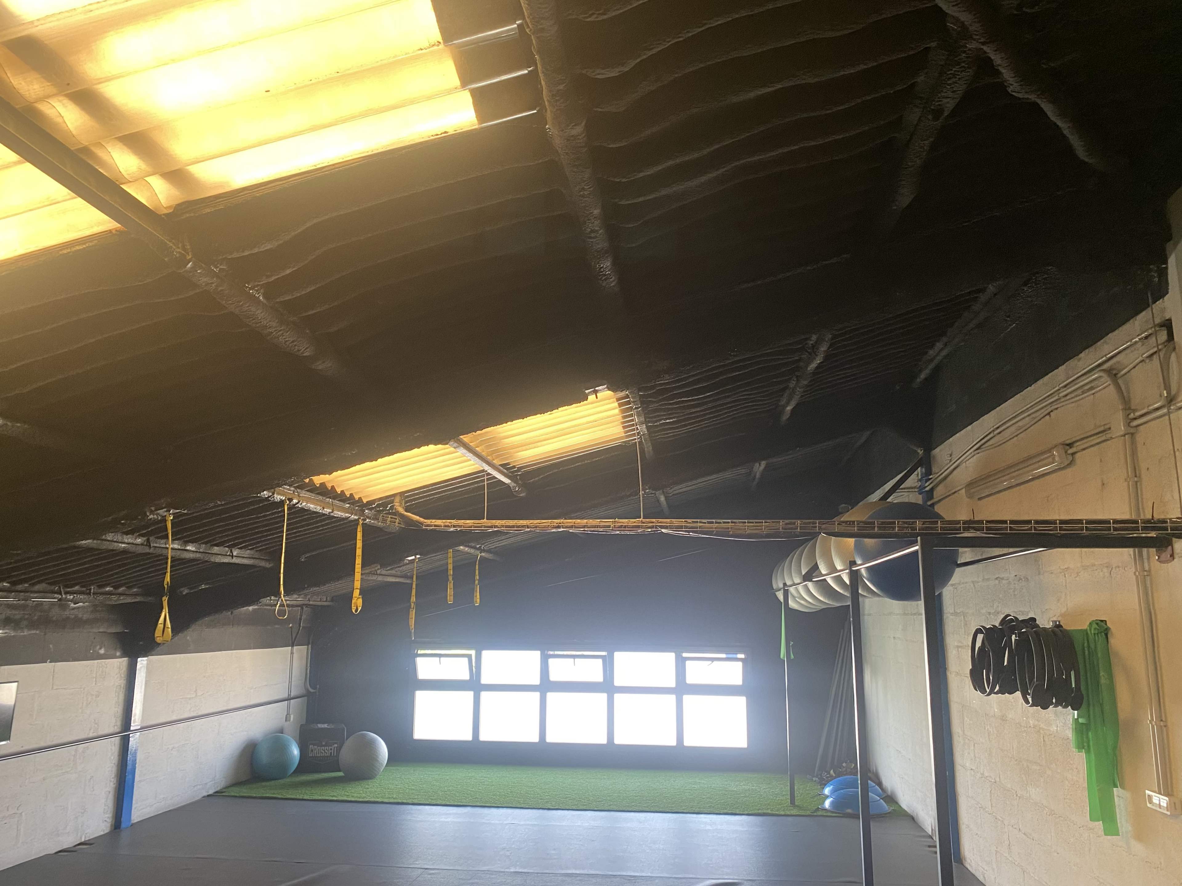 The interior of a gym with a dark ceiling, large windows, exercise balls, and fitness equipment along the wall.